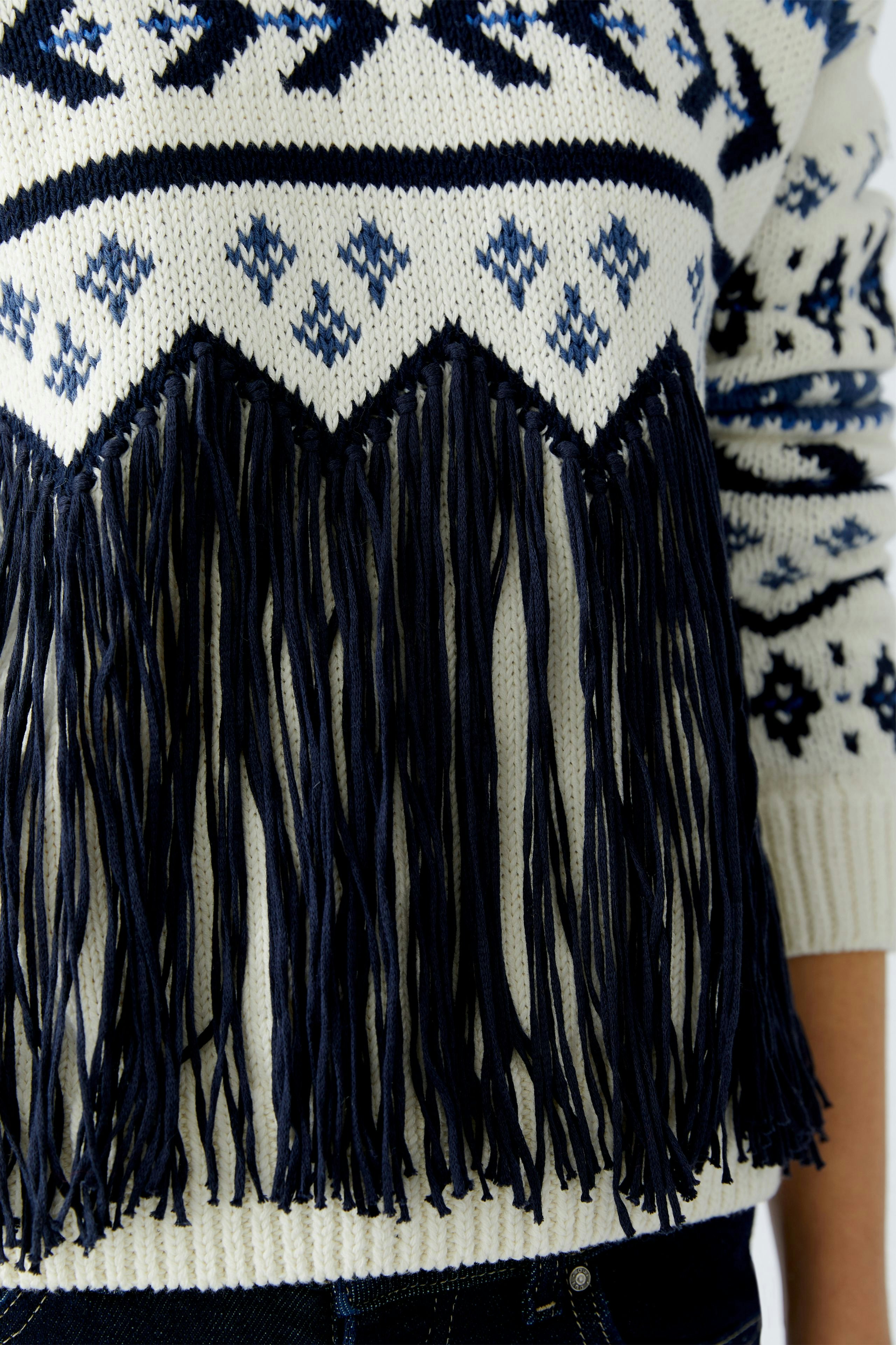 Casual women's pullover: Close-up of a woman in a white pullover with navy fringes and patterns.