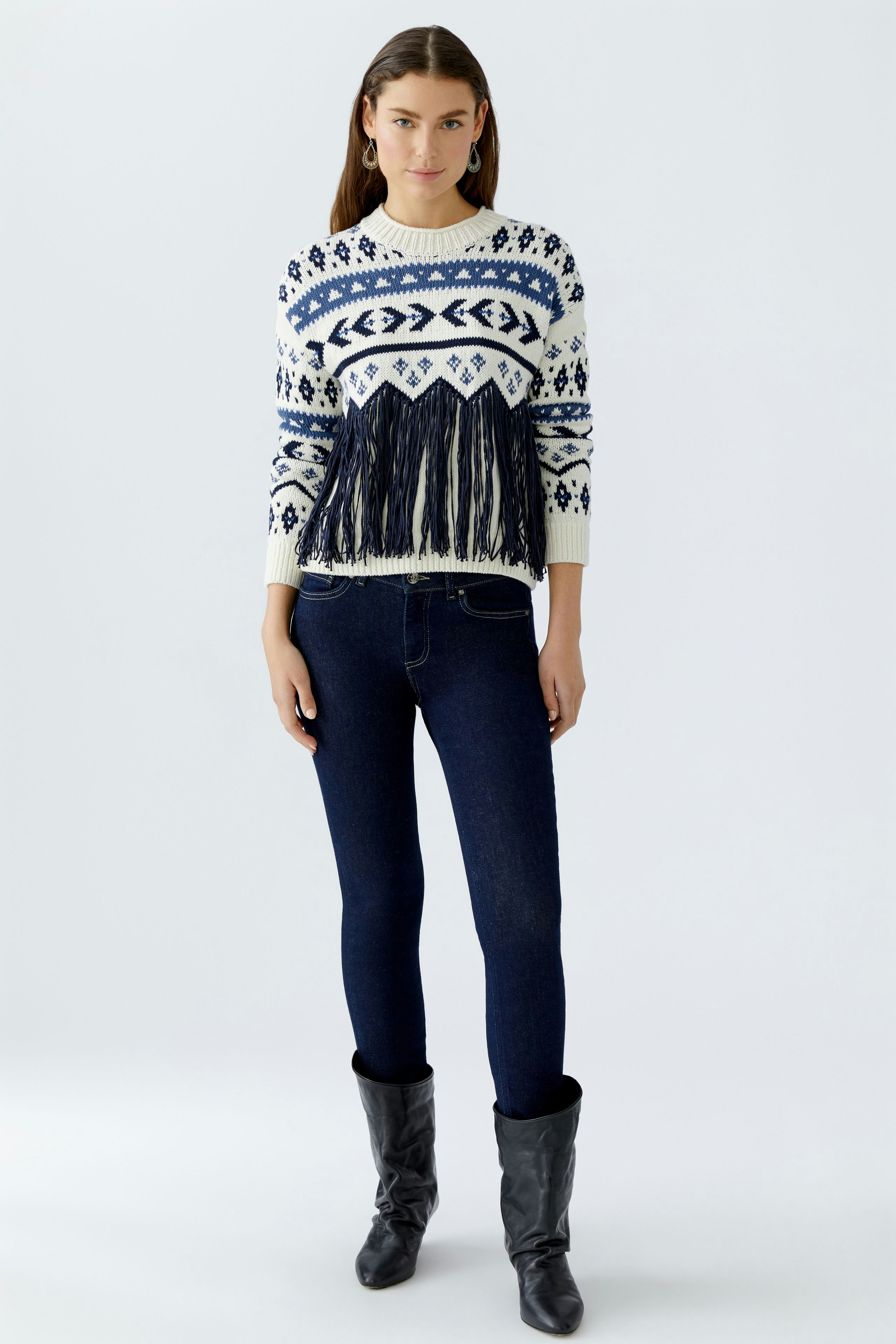 Modern women's pullover: Young woman in a patterned pullover with fringe and dark jeans.
