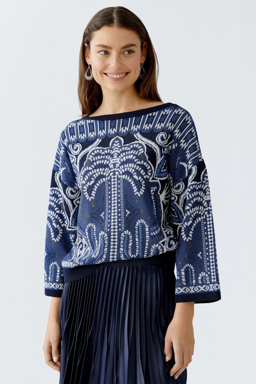 Damen-Pullover: Frau trägt einen blauen, gemusterten Pullover mit weitem Schnitt und lässigem Design.