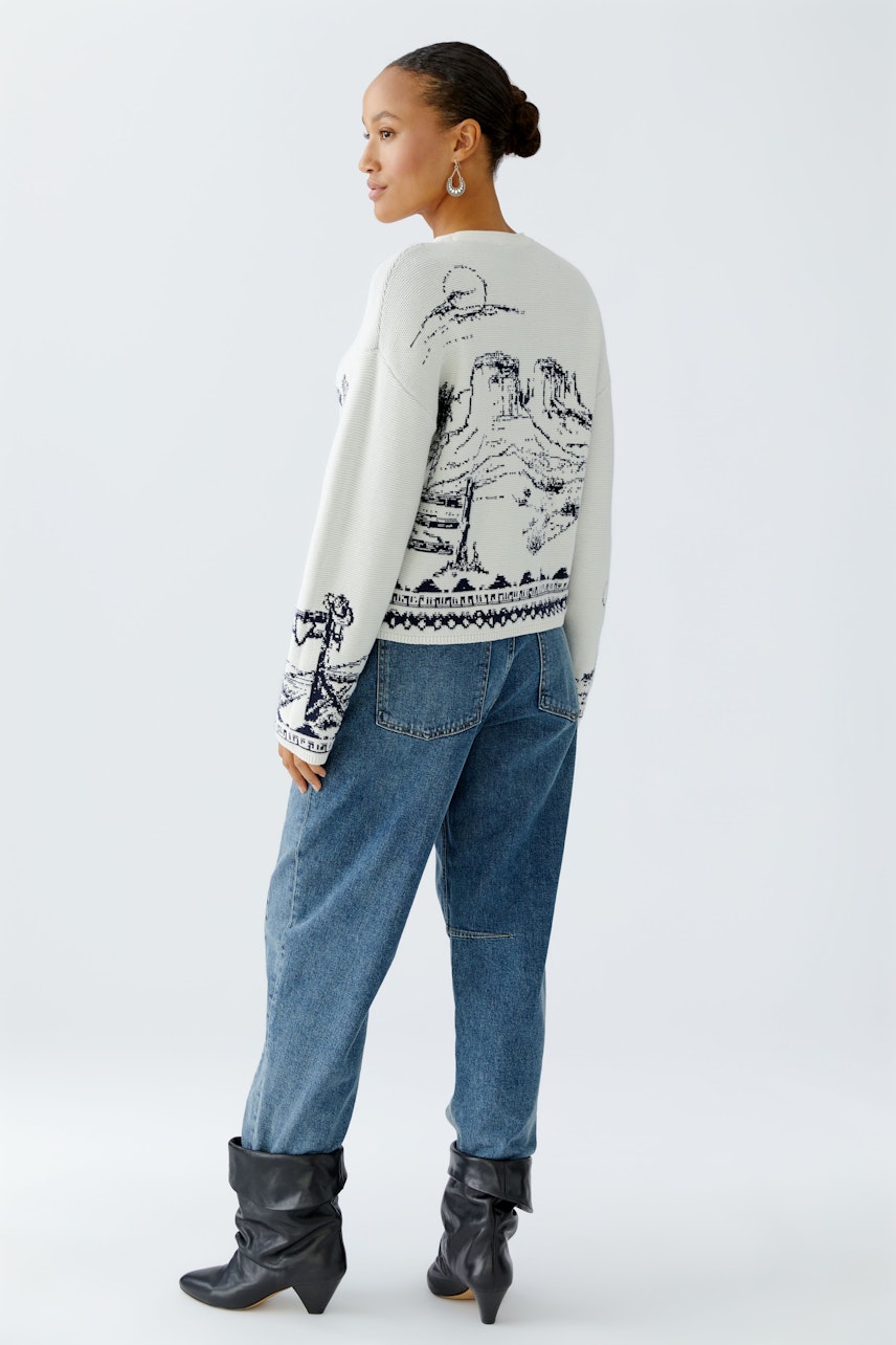 Casual women's pullover: A woman in a cream pullover with a scenic design, paired with relaxed jeans.