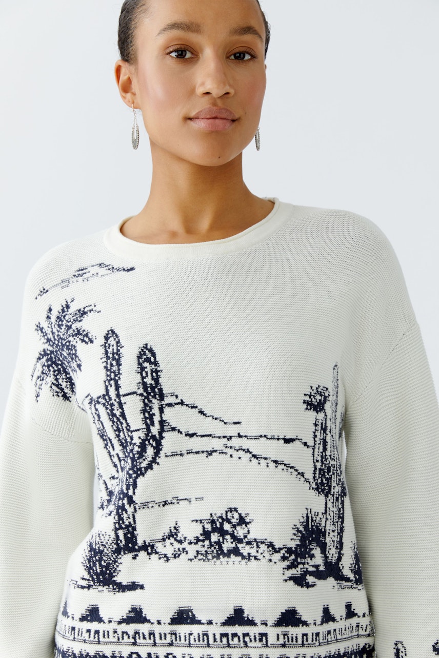 Casual women's pullover: Young woman in a white pullover with cactus print, smiling confidently.