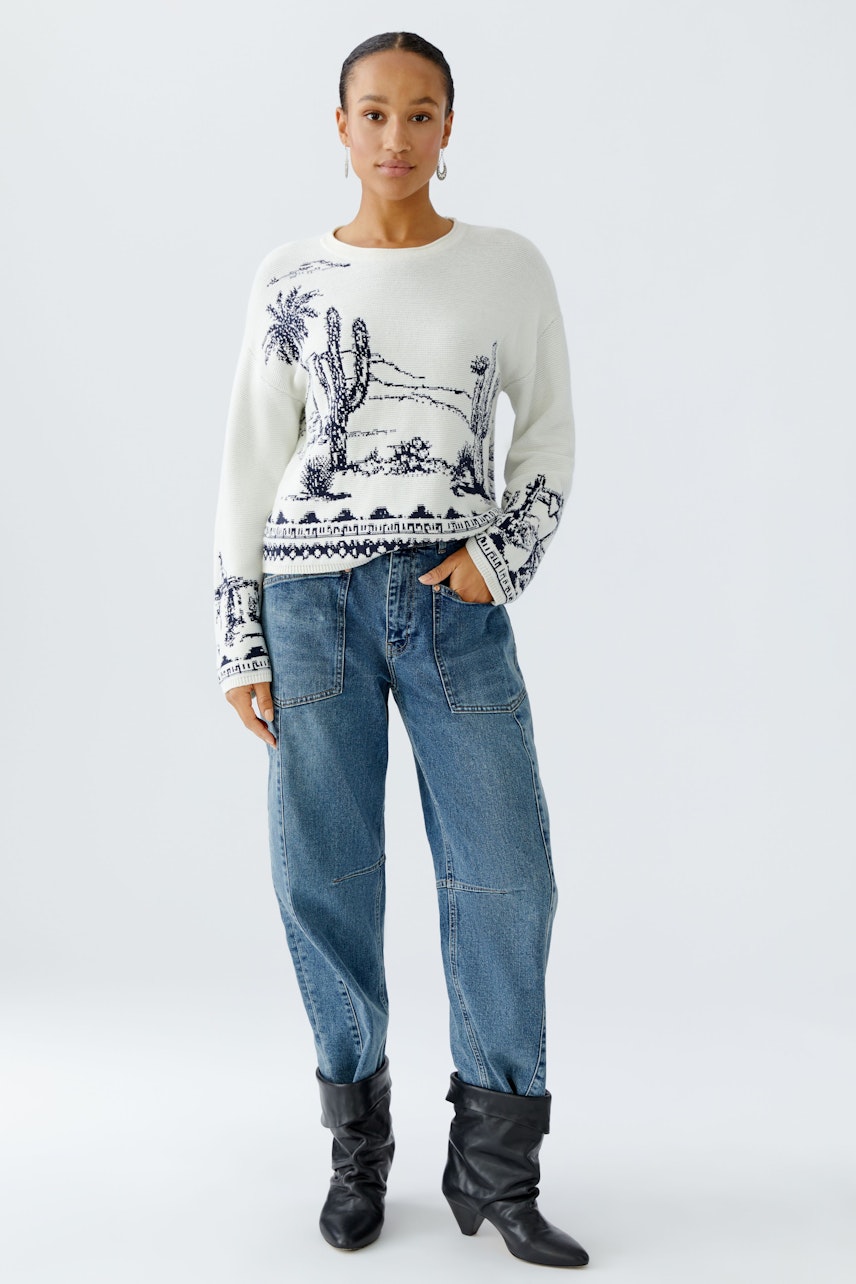 Casual women's pullover: Woman in a white pullover with cactus print and relaxed jeans.