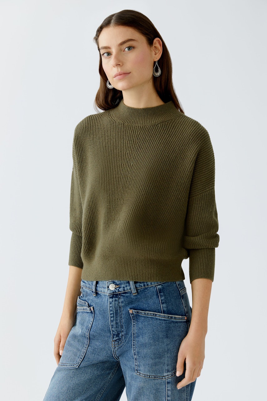 Damen-Pullover: Junge Frau in olivgrünem, strukturiertem Pullover mit lässigen Jeans.
