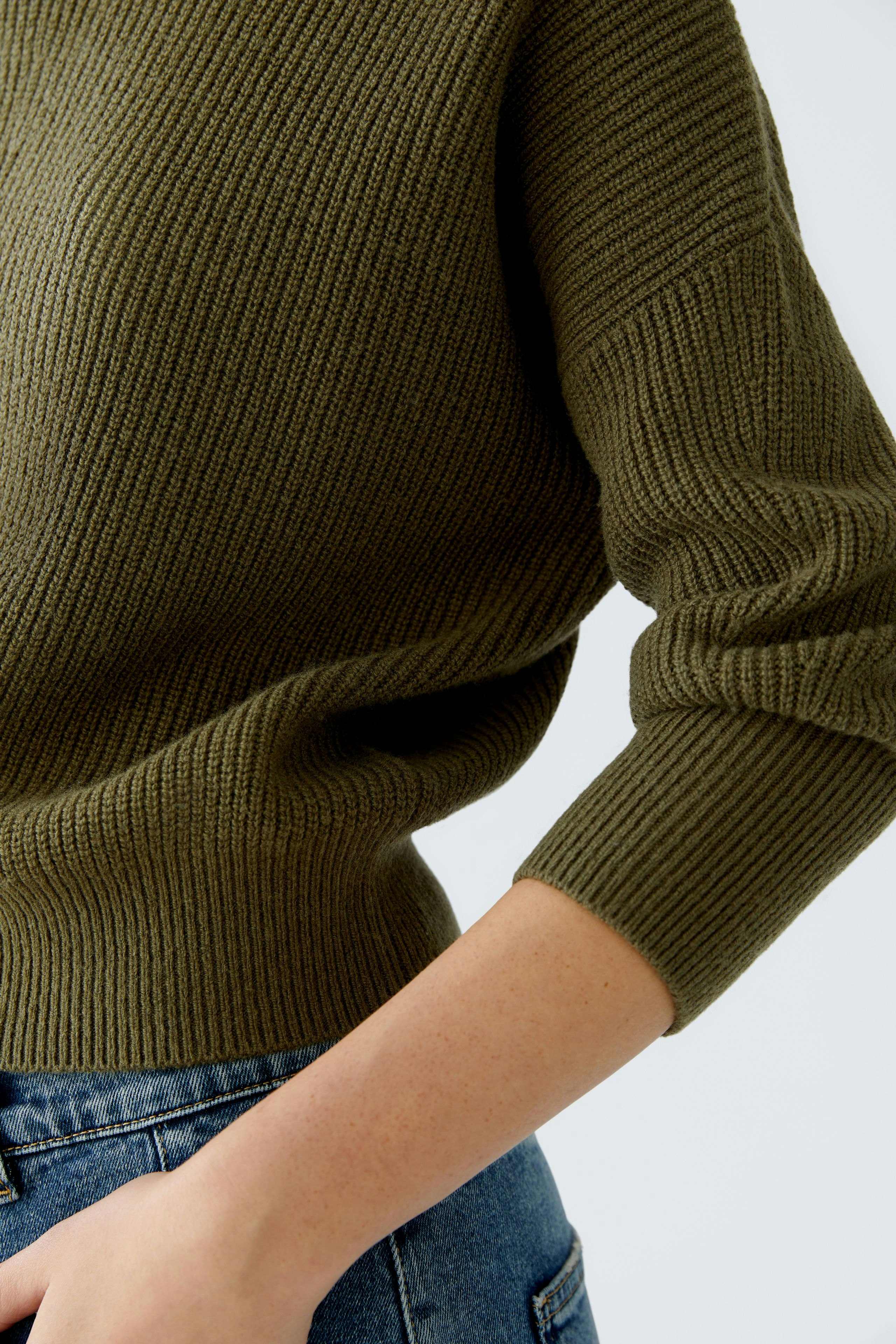 Casual women's pullover: Close-up of a woman wearing a ribbed olive green pullover with three-quarter sleeves.