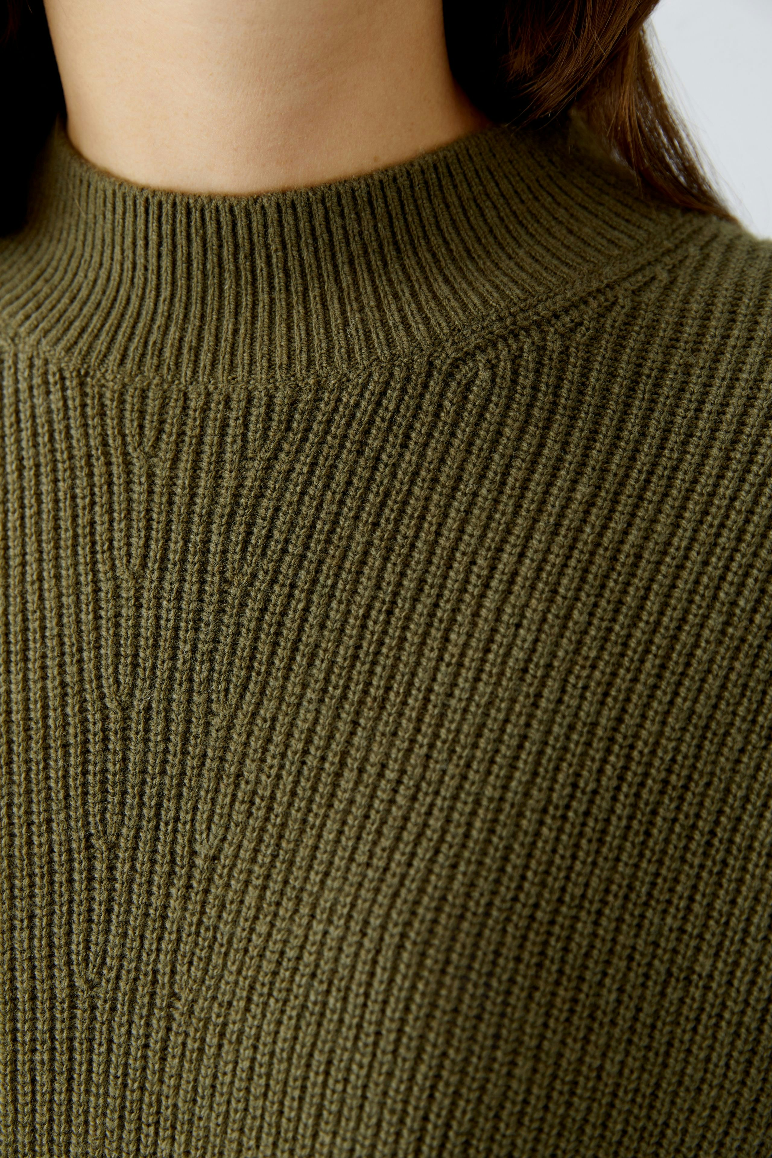 Casual women's pullover: Close-up of a woman in a ribbed olive green pullover with a high neck.