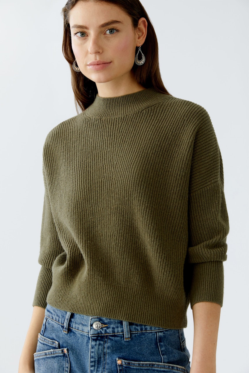 Damen-Pullover: Frau in olivgrünem, strukturiertem Pullover mit hohem Kragen und lässiger Passform.