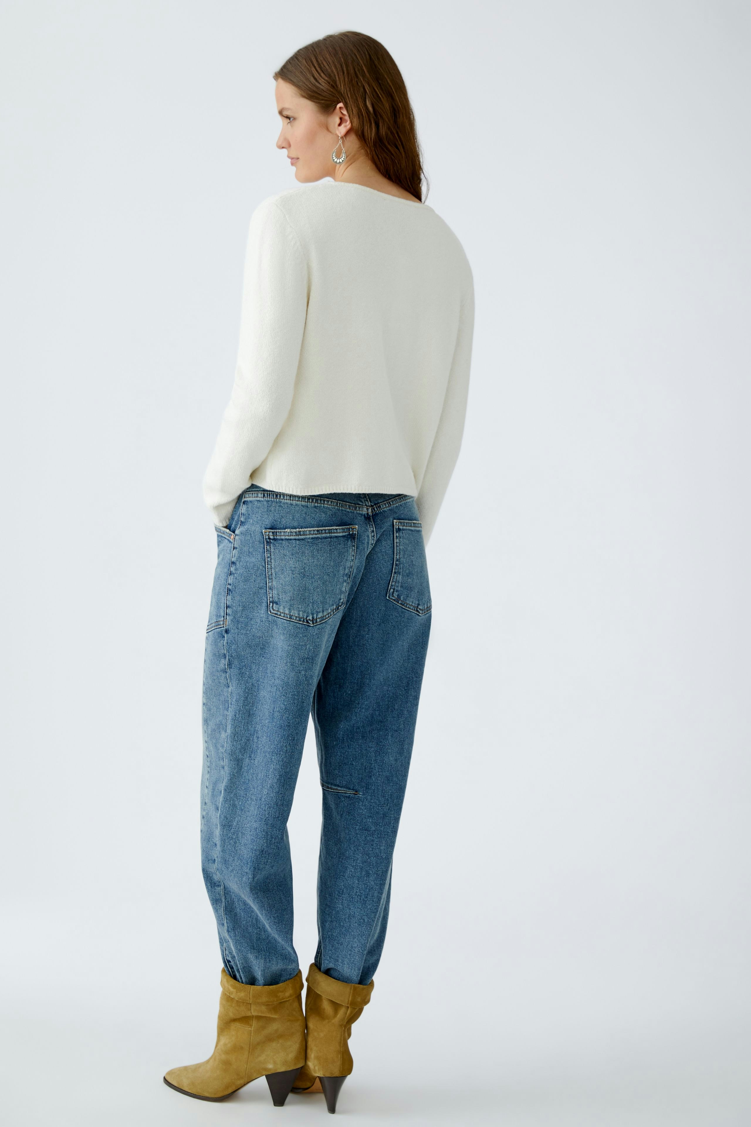 Casual women's cardigan: A woman in a white cardigan and relaxed jeans stands confidently.