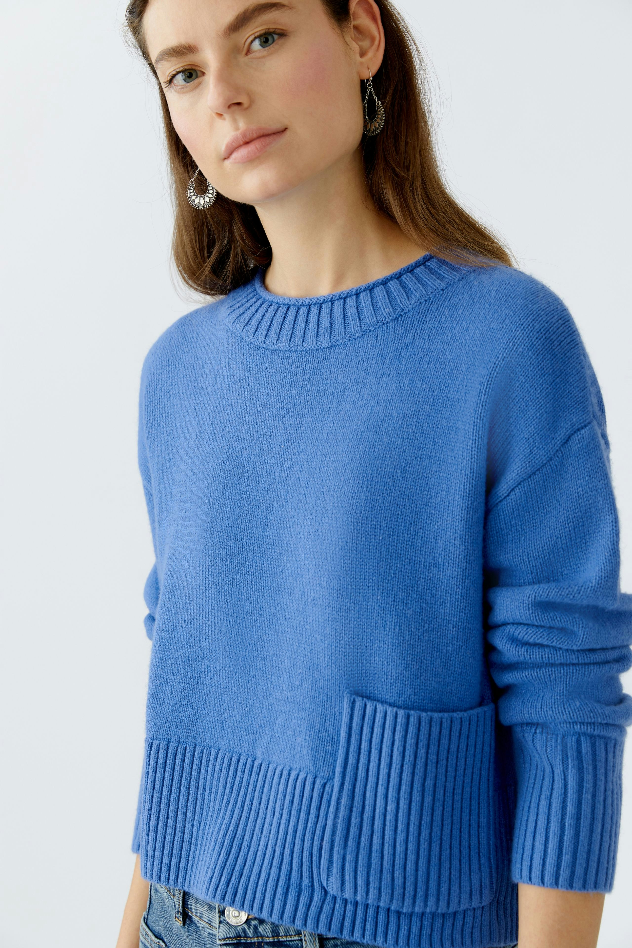 Casual women's pullover: Young woman in a blue pullover with a pocket, styled with relaxed jeans.
