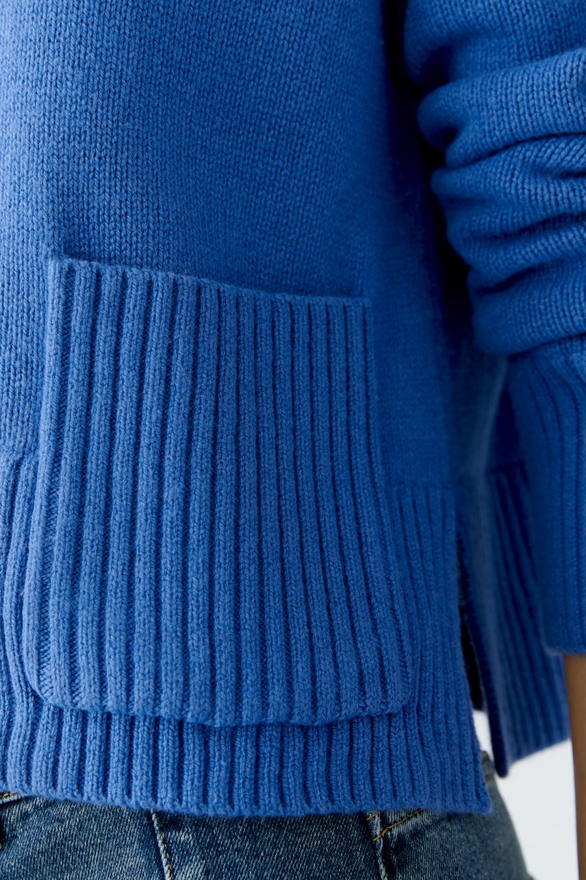 Casual women's pullover: Close-up of a blue knit pullover with ribbed cuffs and pockets.