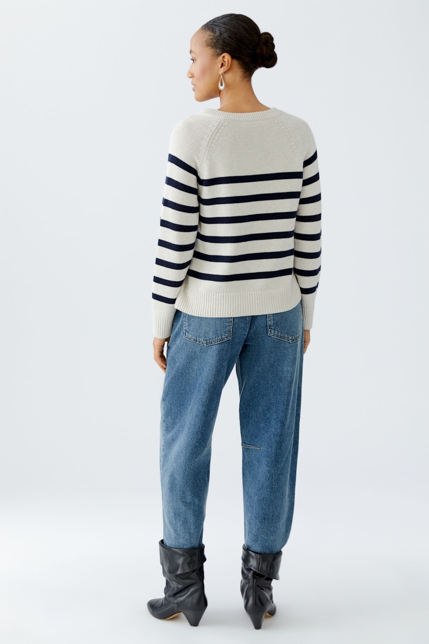 Damen-Pullover: Frau trägt einen gestreiften Pullover in Beige und Marineblau, kombiniert mit lässigen Jeans.