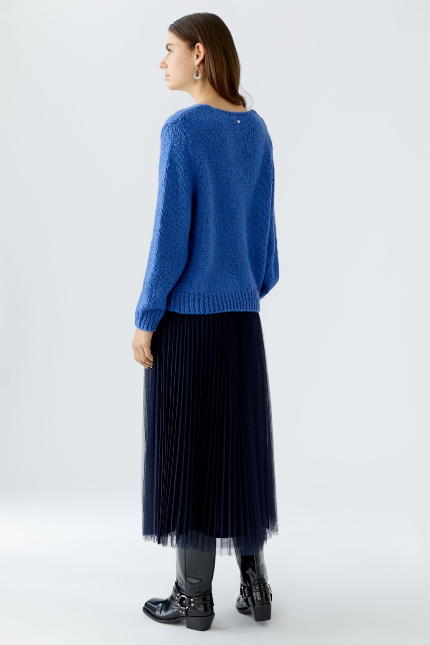 Bequemer Damen-Pullover in Blau, lässig kombiniert mit einem plissierten Rock und Stiefeln.