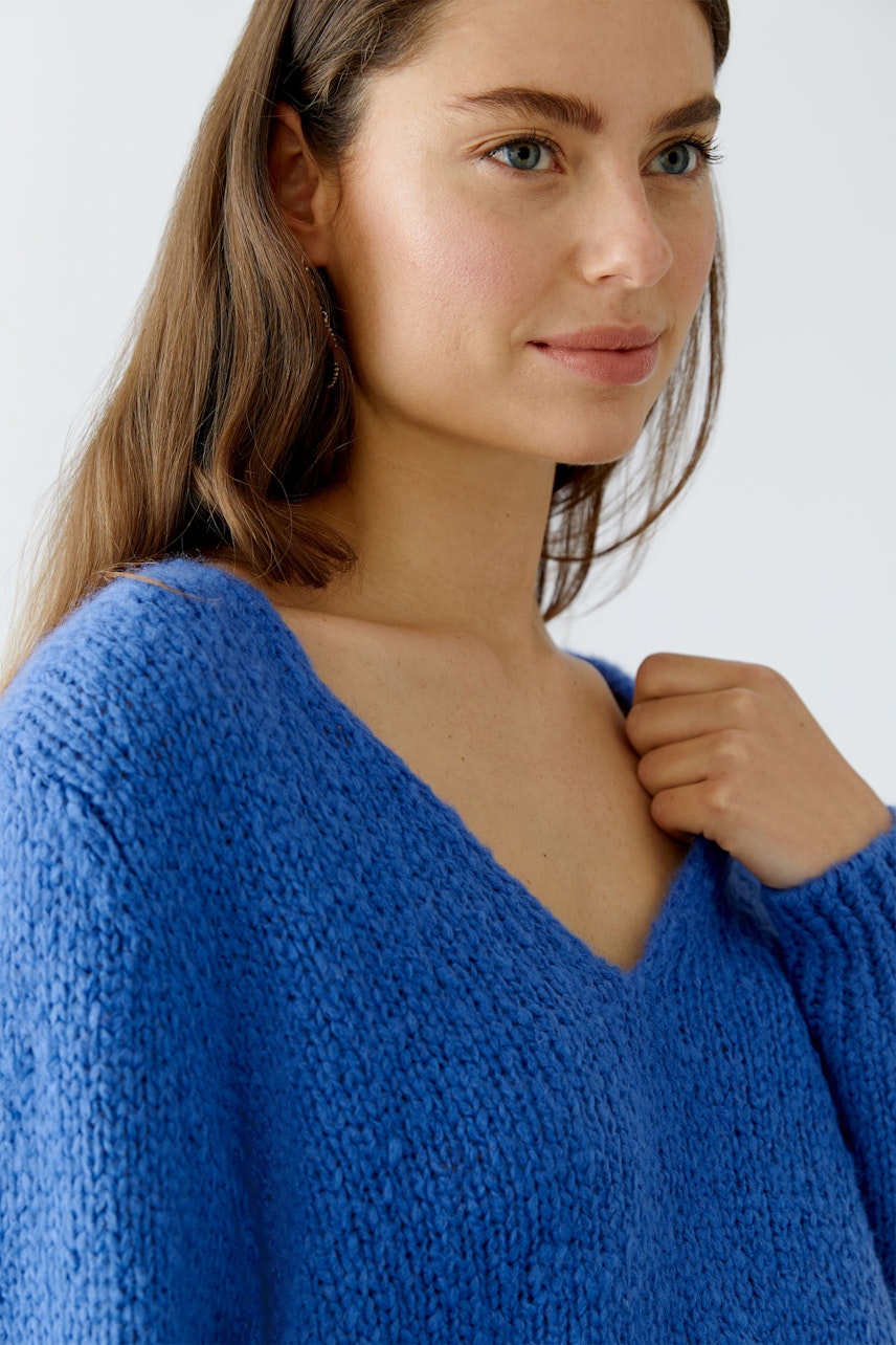 Damen-Pullover: Junge Frau in einem blauen, lockeren Strickpullover mit V-Ausschnitt lächelt freundlich.