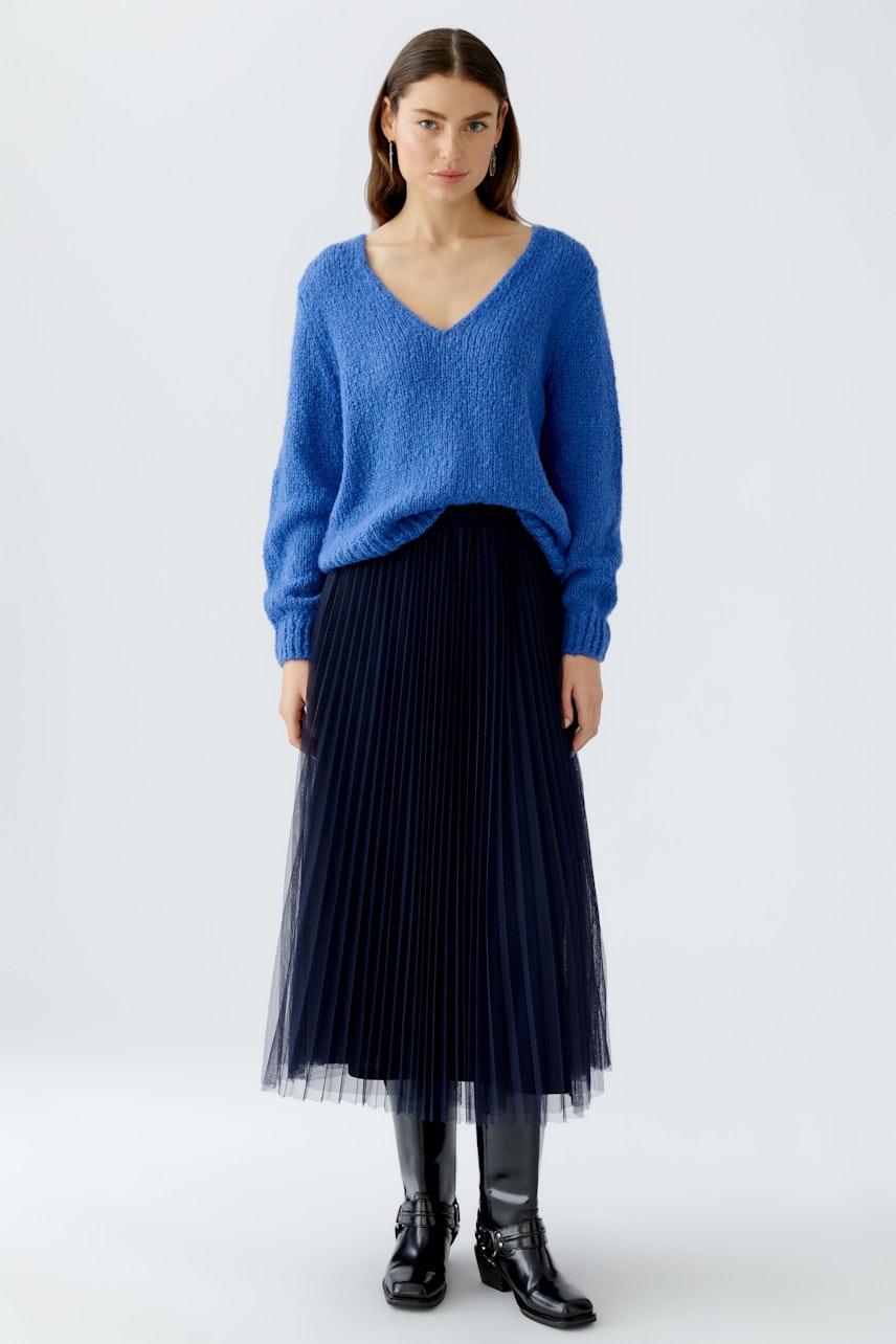 Damen-Pullover: Frau in blauem, weichem Strickpullover mit V-Ausschnitt und plissiertem Rock.