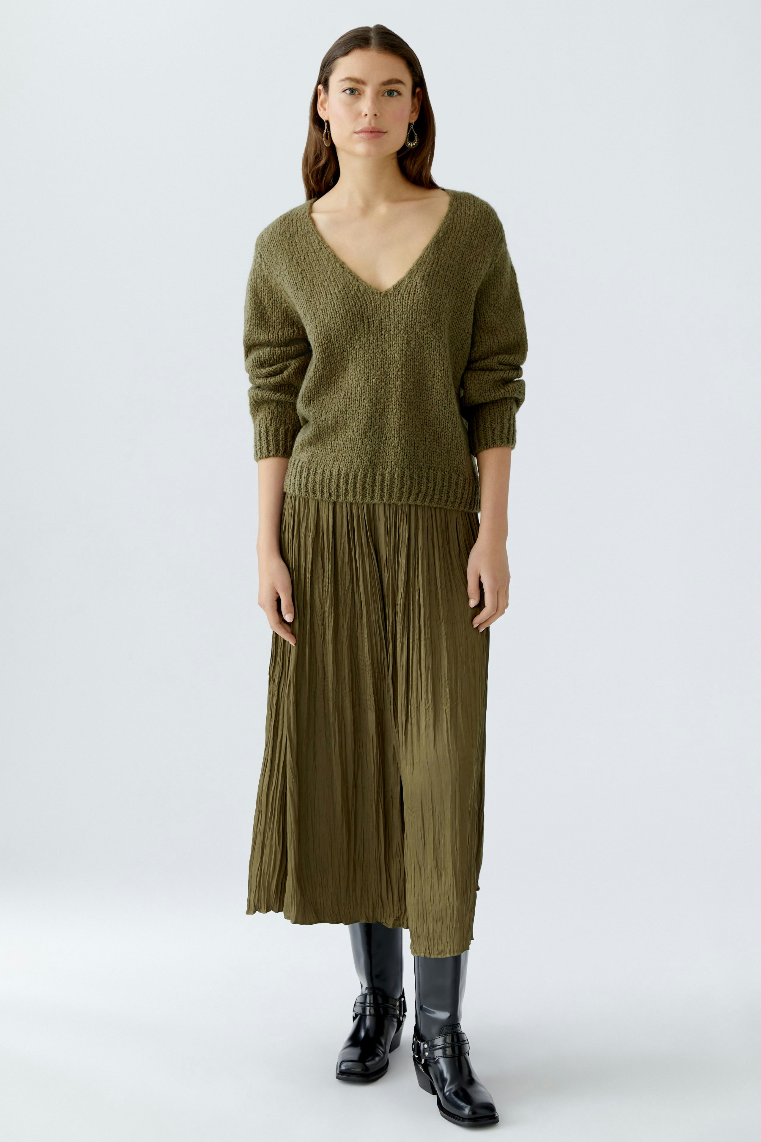 Casual women's pullover: A woman in an olive green V-neck pullover paired with a pleated skirt.