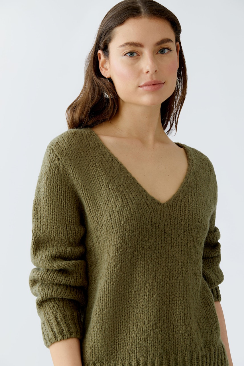 Damen-Pullover: Frau in olivgrünem, grob gestricktem Pullover mit V-Ausschnitt und lässigen Ärmeln.