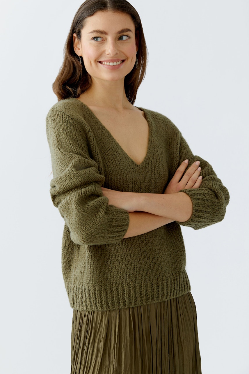 Damen-Pullover: Frau in olivgrünem Strickpullover mit V-Ausschnitt und lässigen Puffärmeln lächelt.