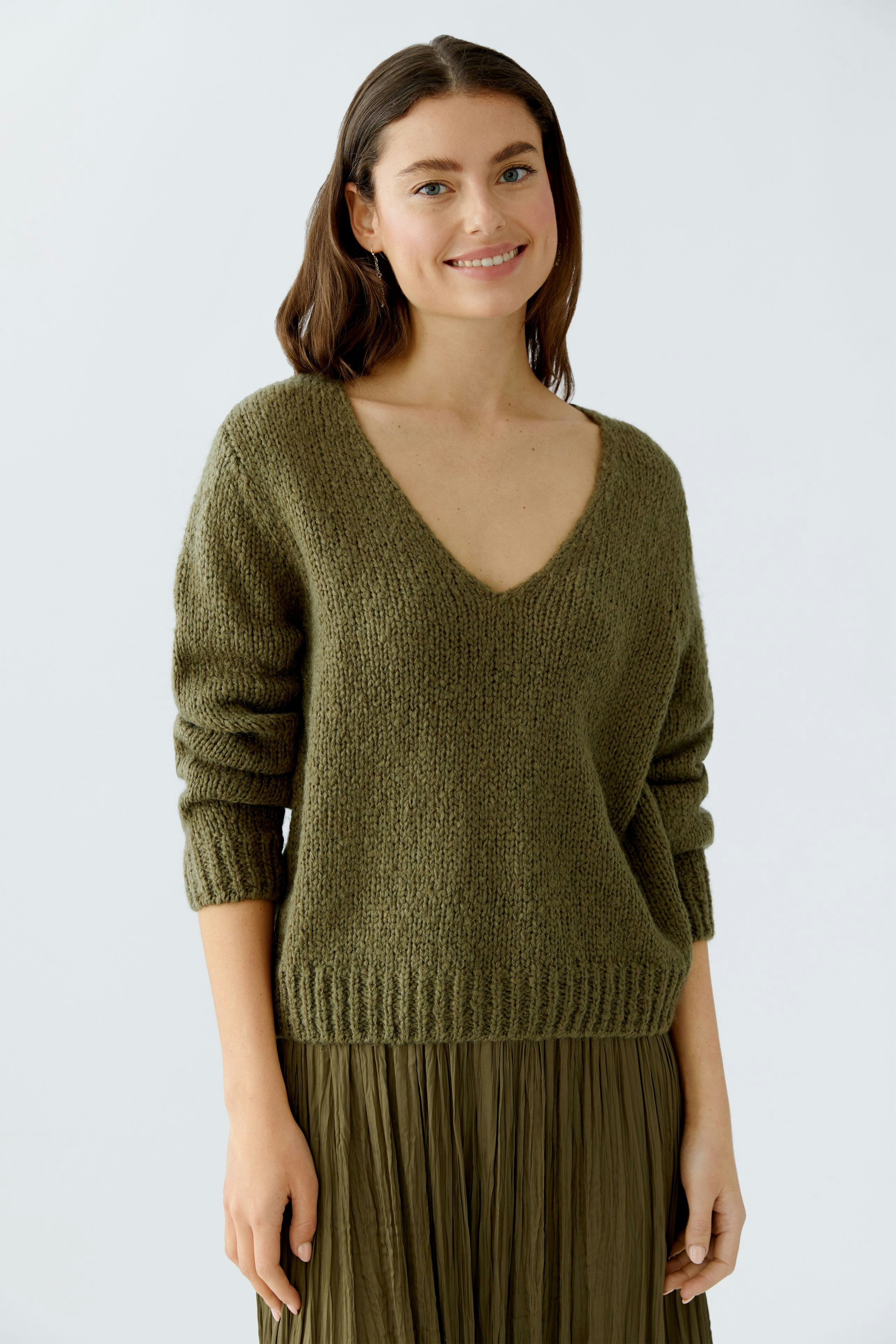 Casual women's pullover: Smiling woman in a green V-neck pullover with relaxed fit.