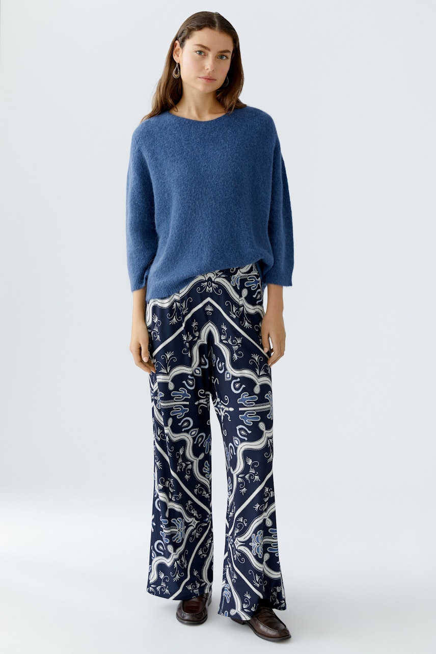 Damen-Pullover: Junge Frau im blauen, lässigen Strickpullover mit weitem Schnitt und gemusterter Hose.