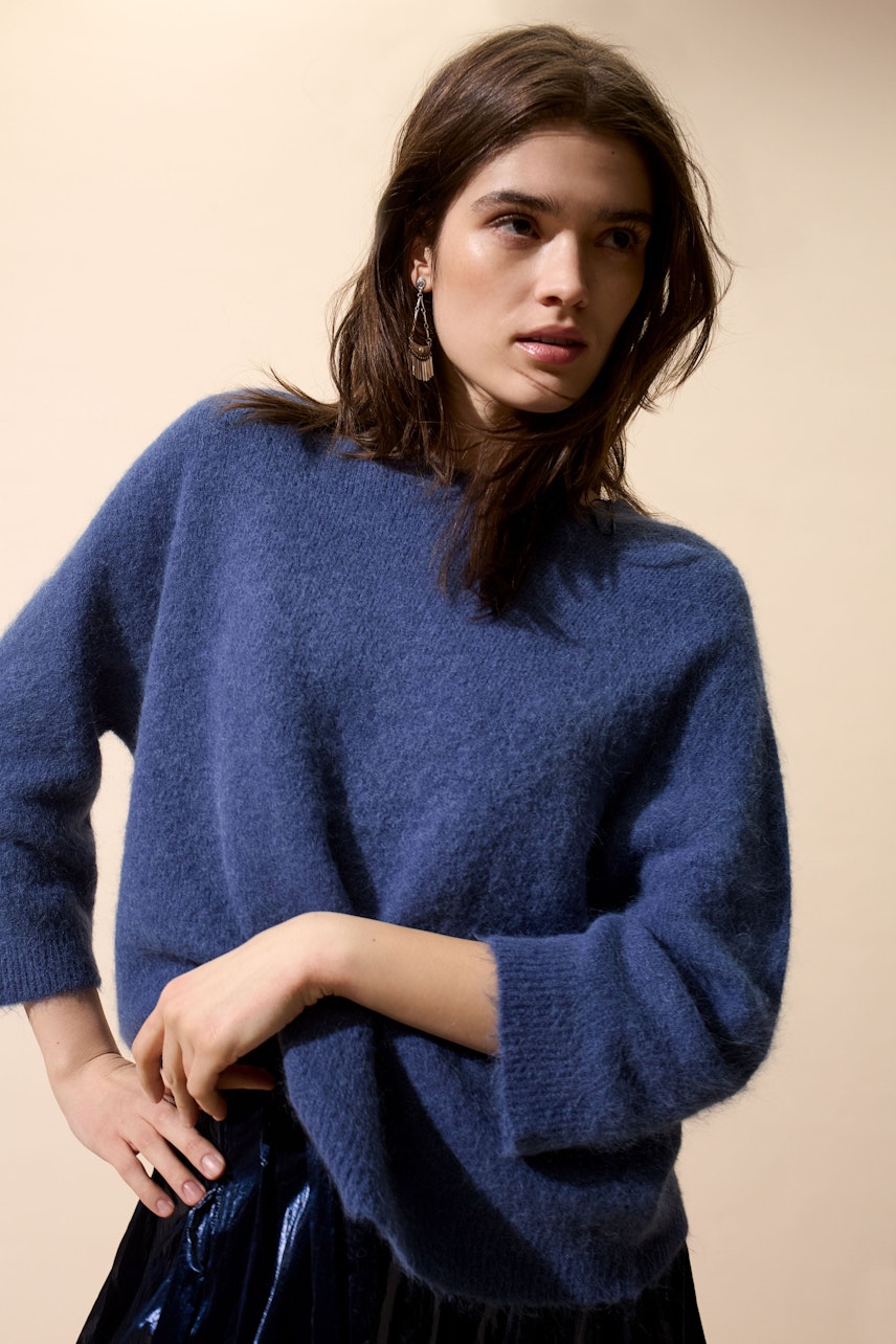 Damen-Pullover: Junge Frau in einem blauen, lässigen Strickpullover mit weiten Ärmeln.