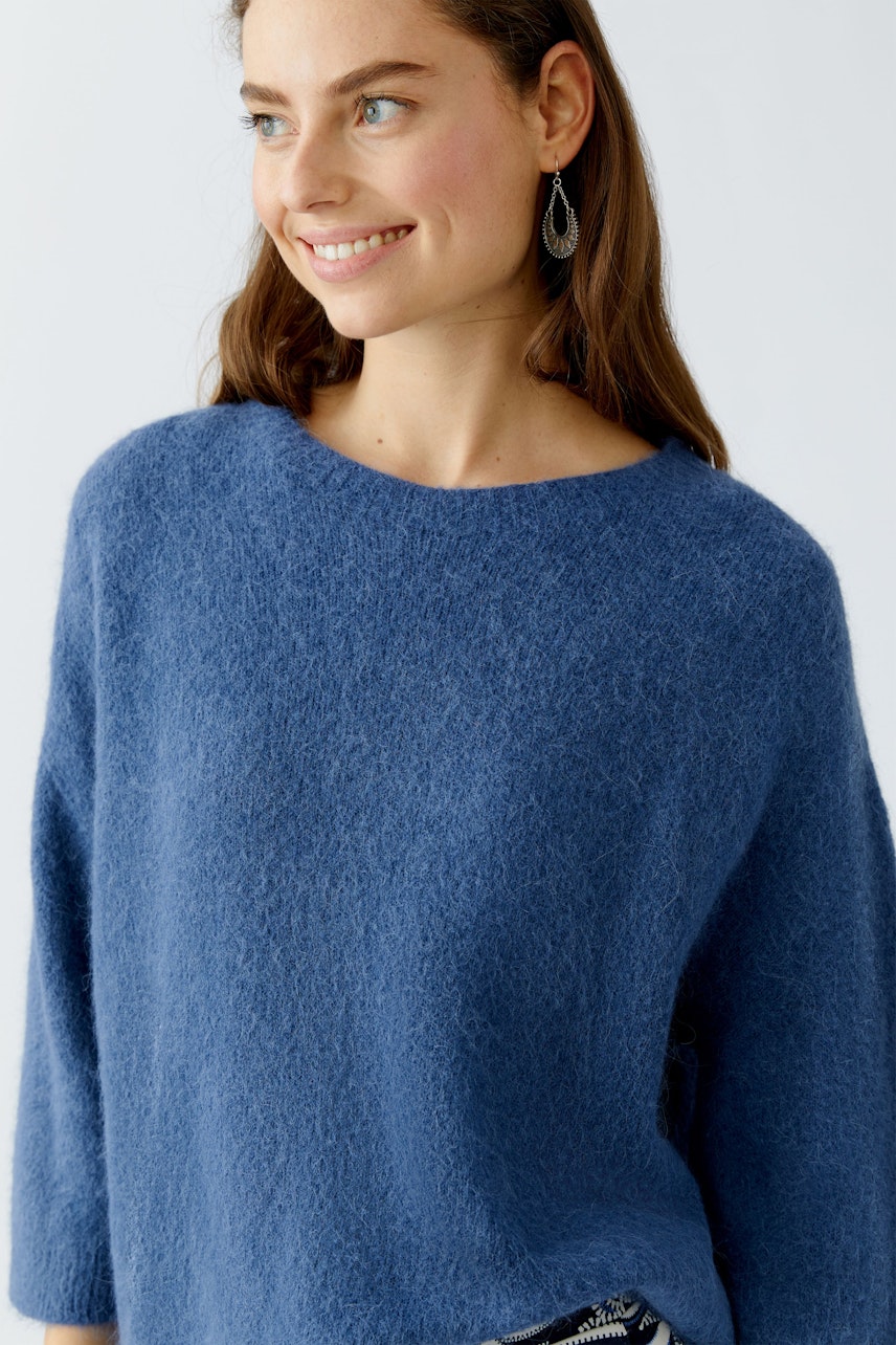 Damen-Pullover: Junge Frau in einem blauen, weichen Strickpullover mit Rundhalsausschnitt lächelt.