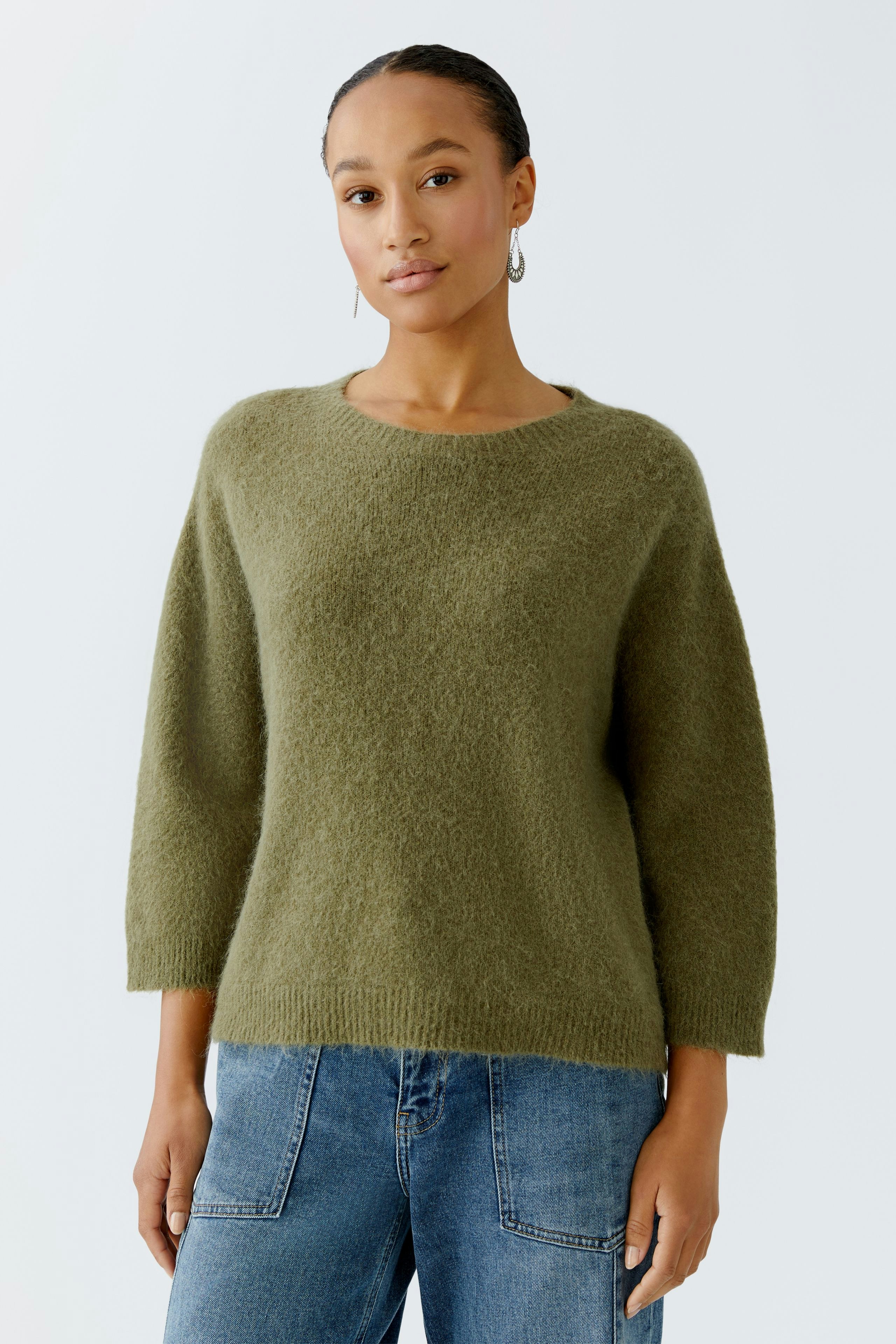 Damen-Pullover: Frau trägt einen olivgrünen, lässigen Pullover mit 3/4-Ärmeln und kombiniert ihn mit Jeans.