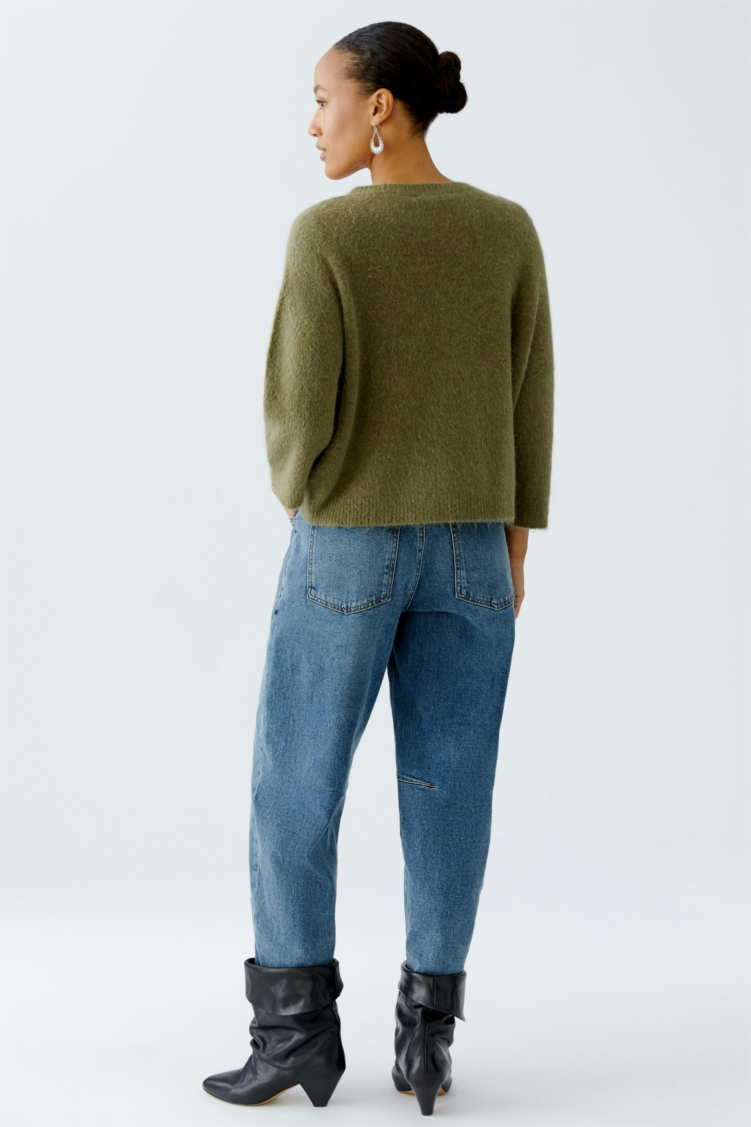 Damen-Pullover: Frau in grünem, lässigem Strickpullover mit lockerer Passform und Jeans.