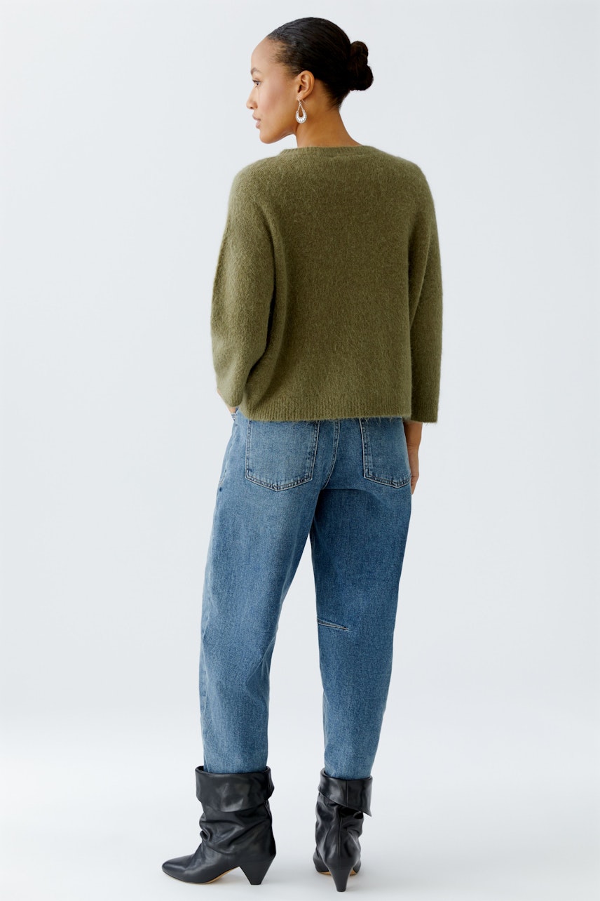 Damen-Pullover: Frau in grünem, lässigem Strickpullover mit lockerer Passform und Jeans.