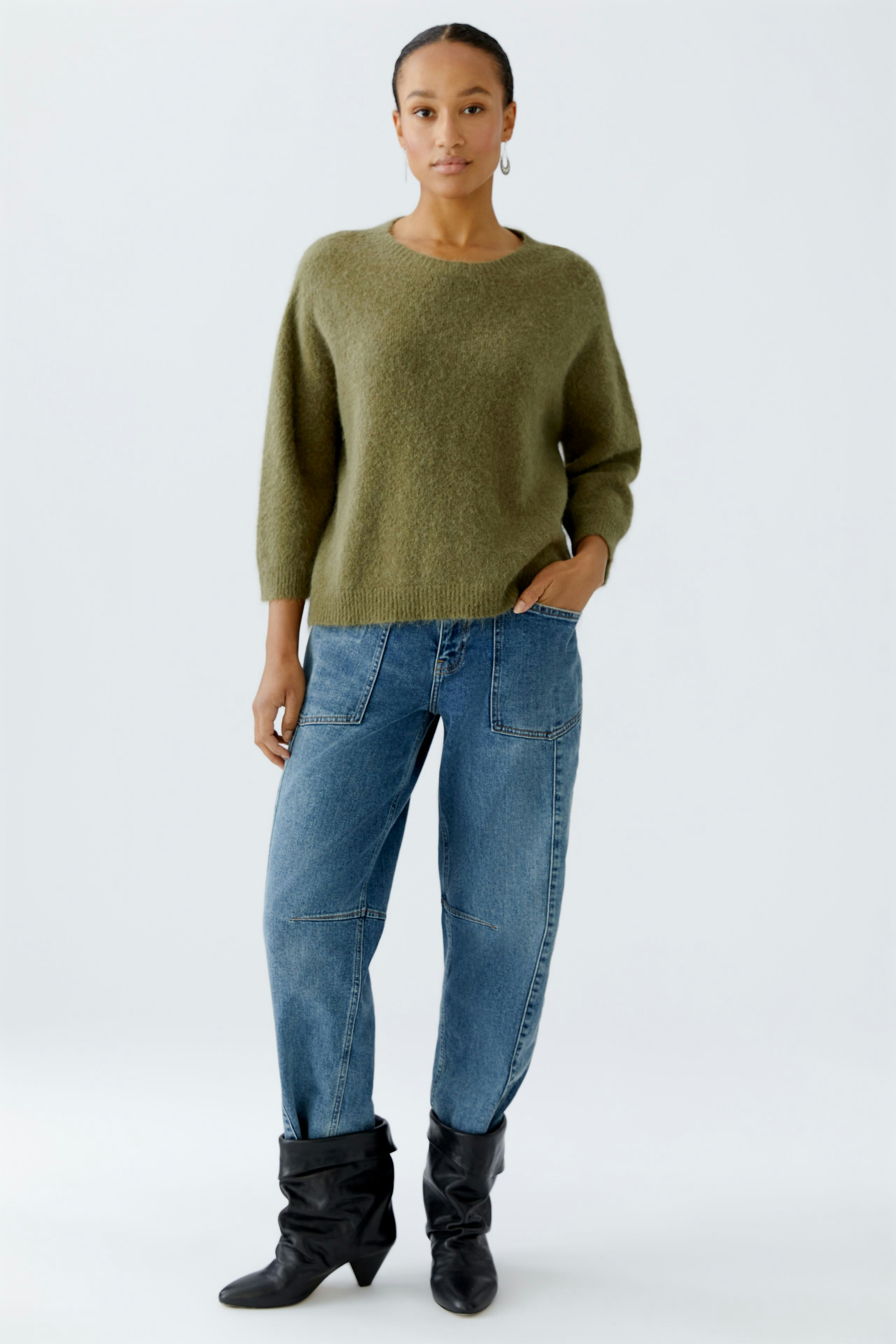Damen-Pullover: Frau in grünem, lässigem Strickpullover mit lockerer Passform und Jeans.