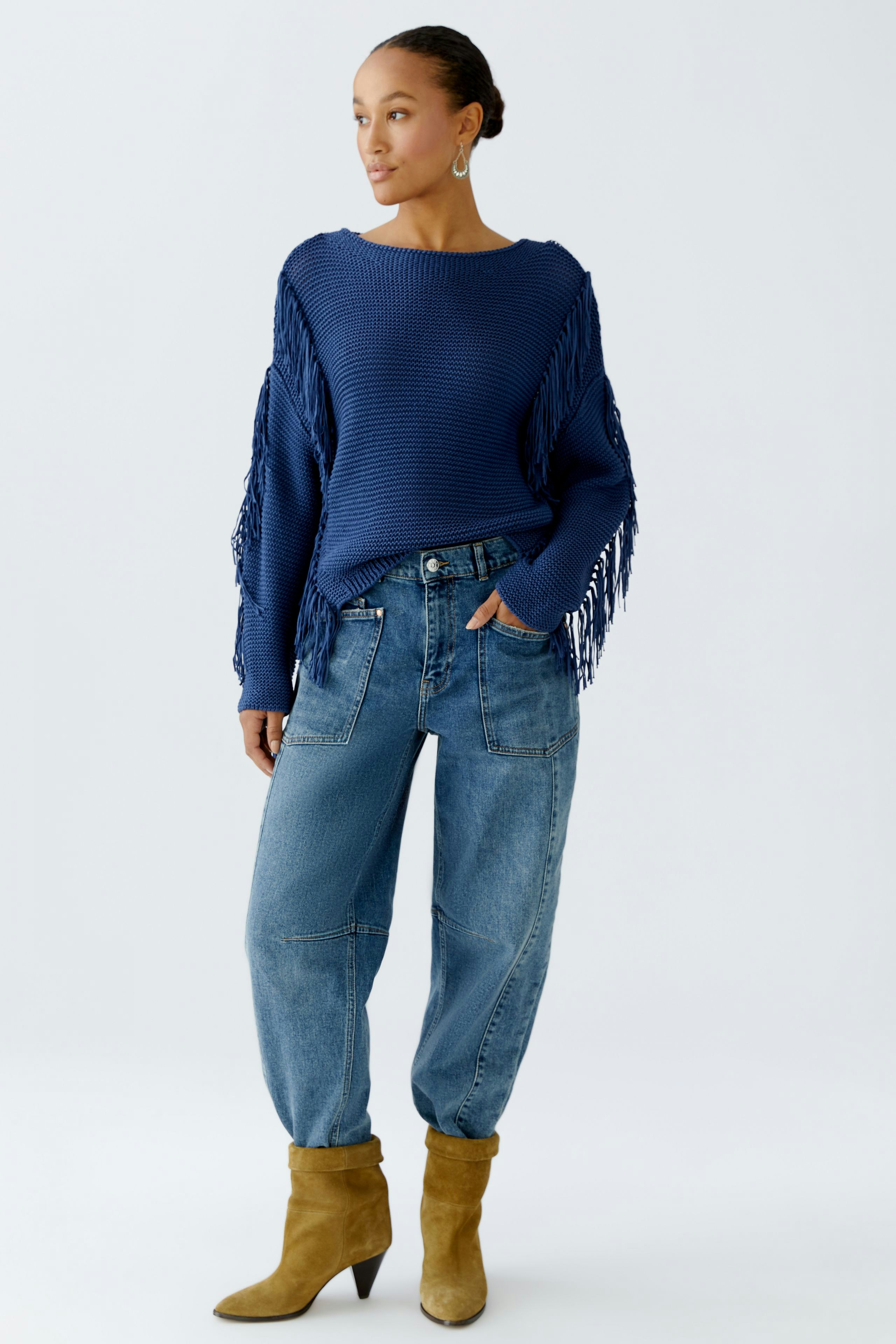 Damen-Pullover in Blau mit Fransen, kombiniert mit lässigen Jeans und Stiefeln.