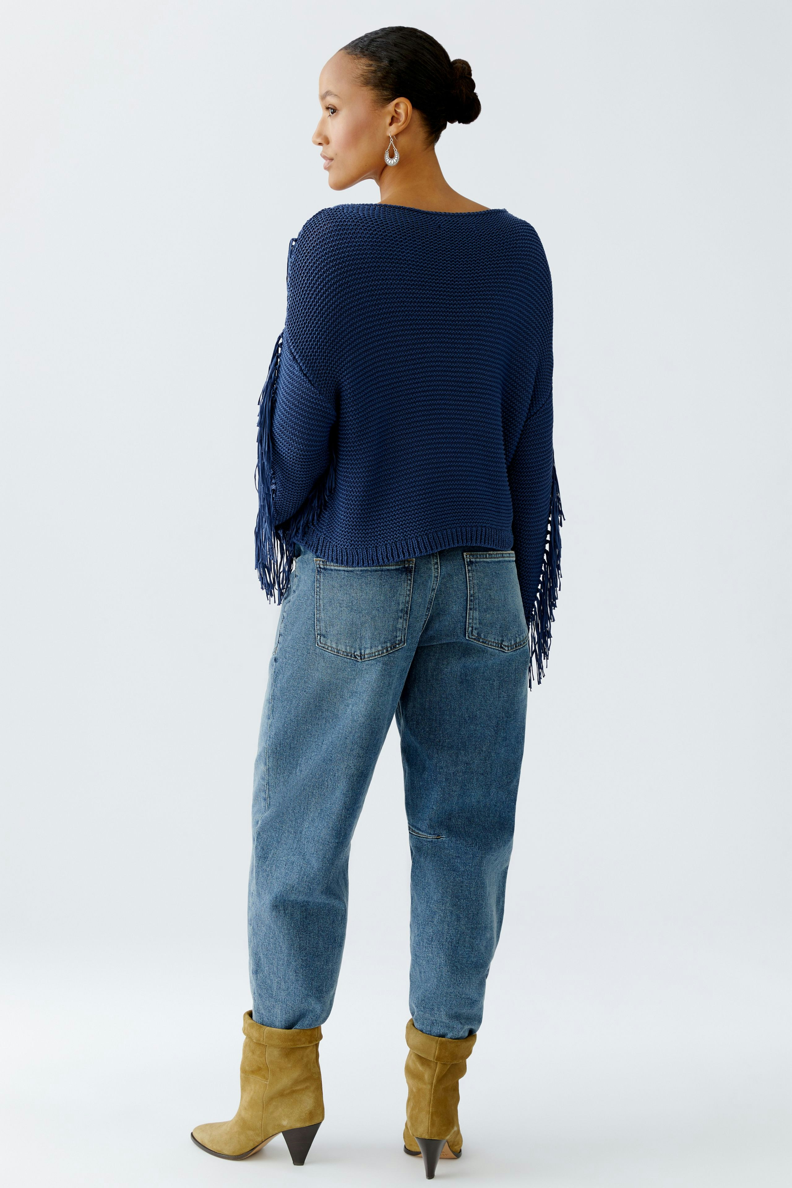 Damen-Pullover: Frau in blauem Strickpullover mit Fransen und lässigen Jeans, von hinten zu sehen.