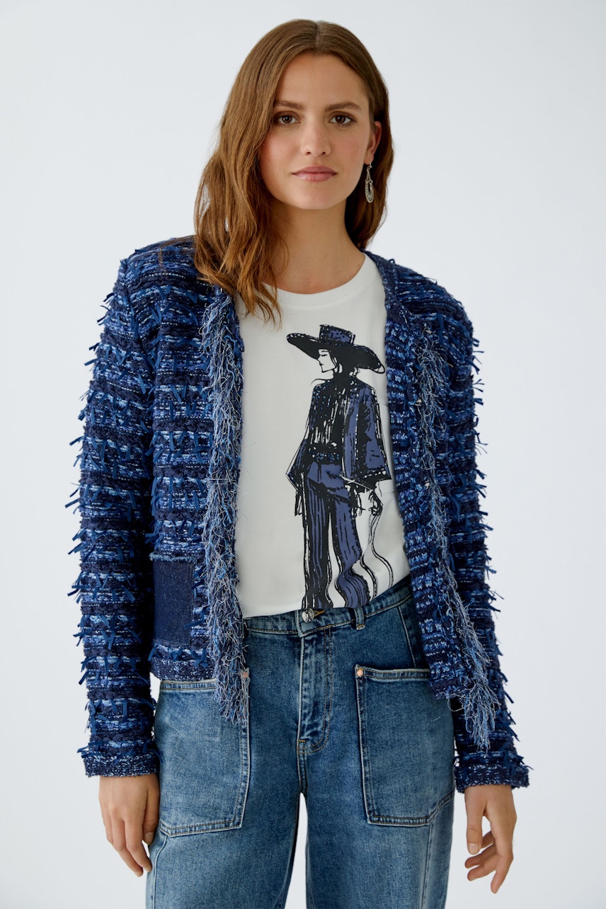 Damen-Strickjacke: Frau in blauer Strickjacke mit Fransen über einem T-Shirt und Jeans.
