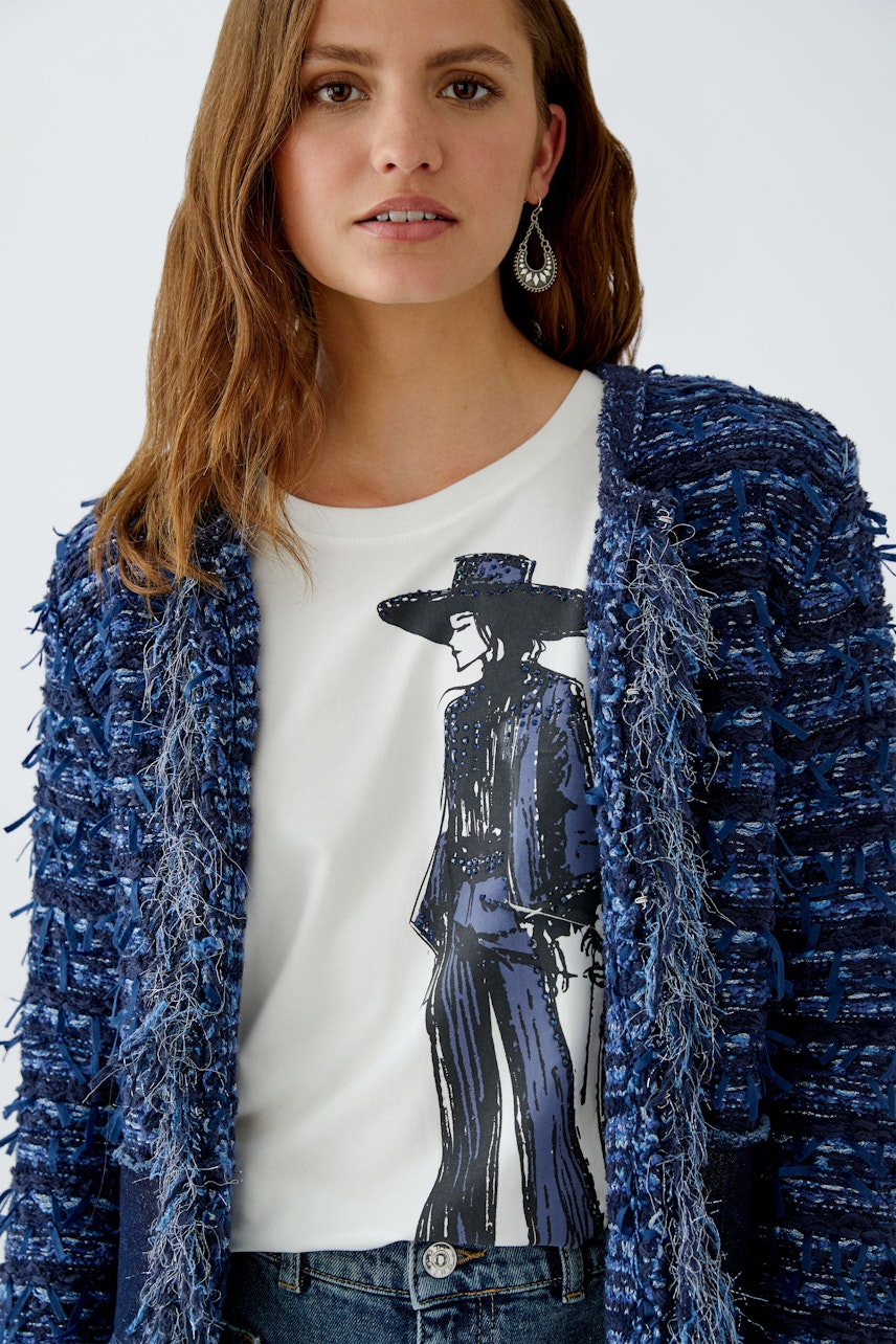Damen-Strickjacke in Blau mit fransigem Design, kombiniert mit einem weißen T-Shirt und lässigen Jeans.