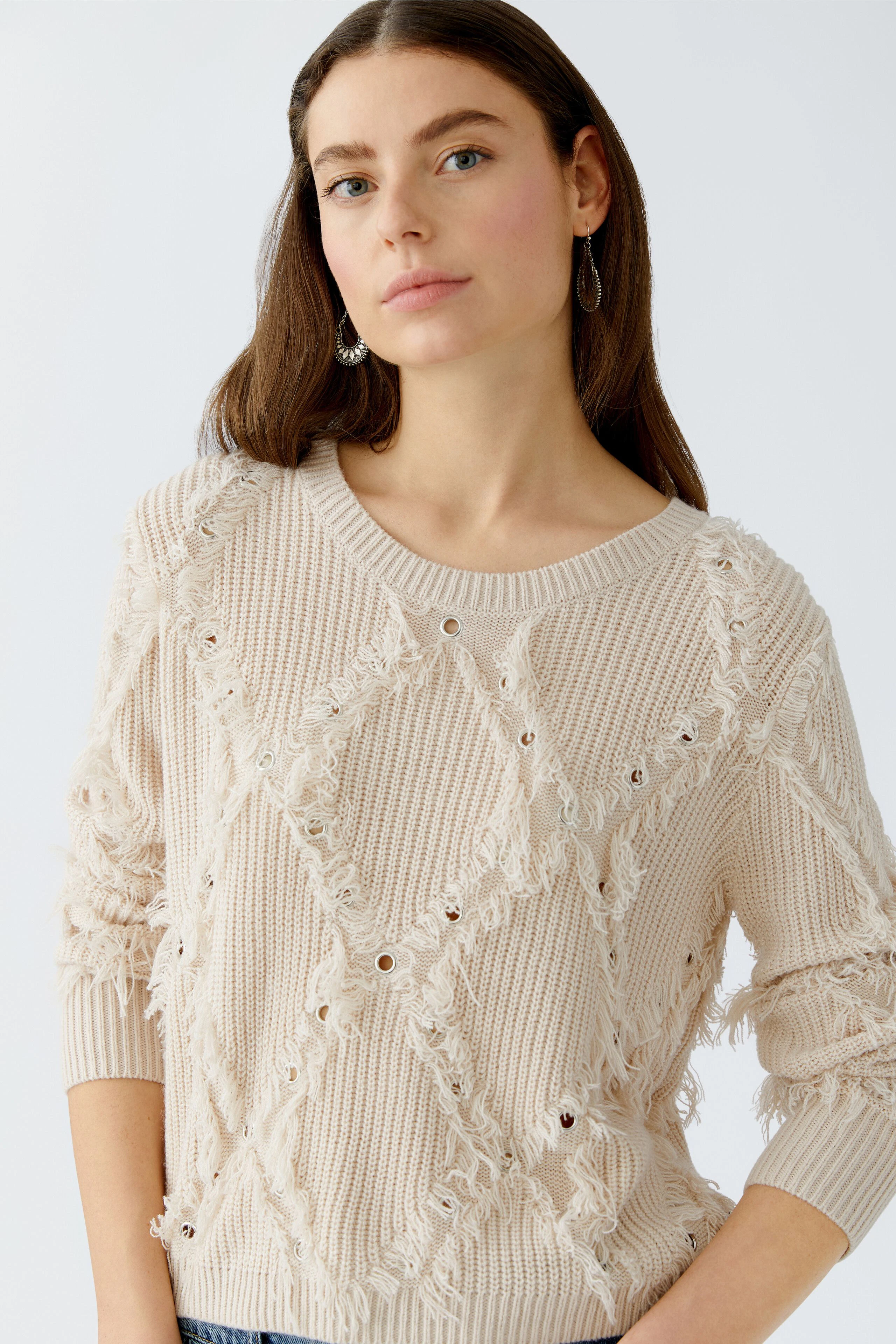 Casual women's pullover: A woman in a light beige pullover with a textured design and frayed details.