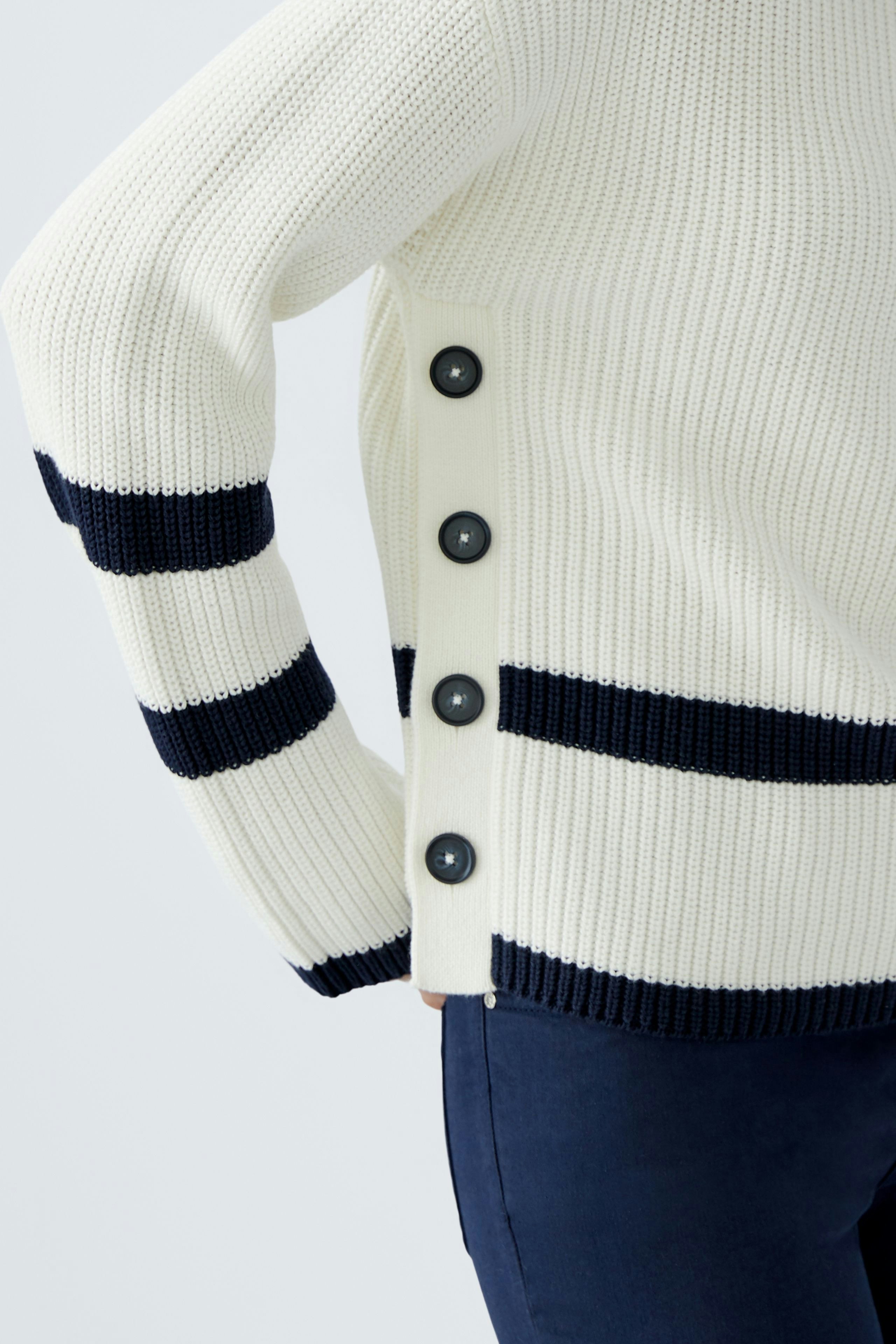 Casual women's pullover: A woman in a cream pullover with navy stripes and button details.