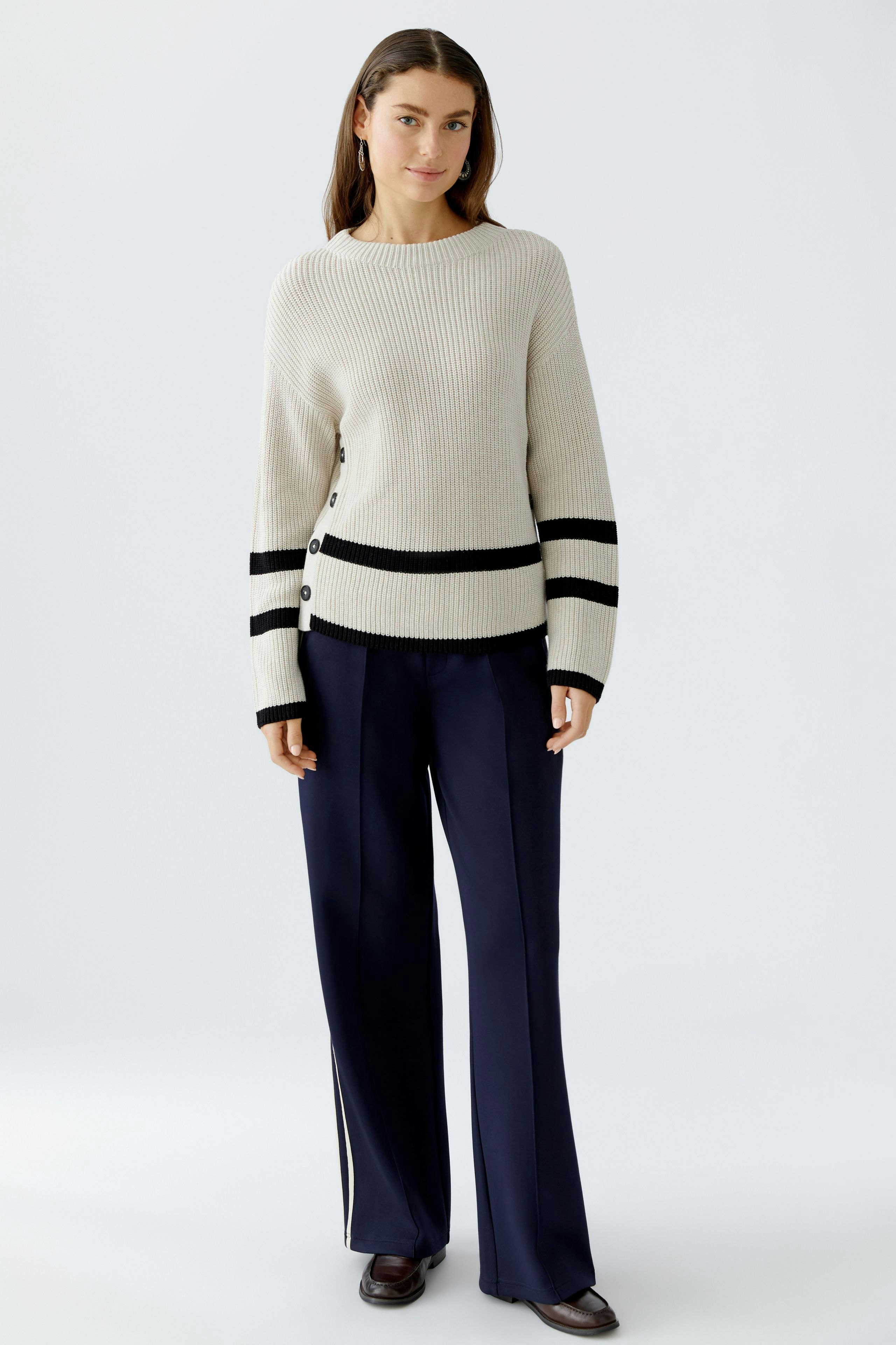 Casual women's pullover: Young woman in a cream ribbed pullover with black stripes and buttons.