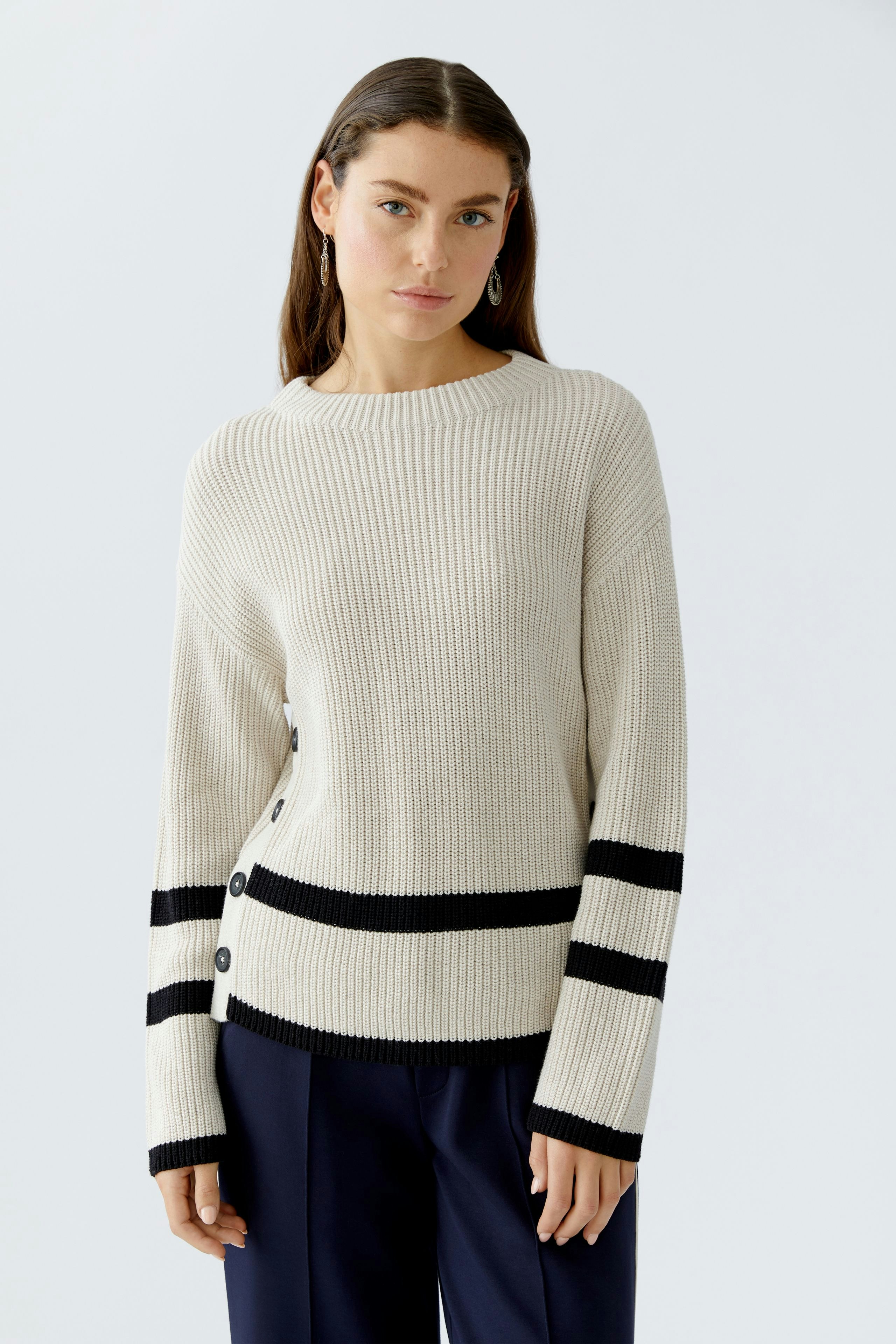 Casual women's pullover: A woman in a cream ribbed pullover with black stripes and button details.