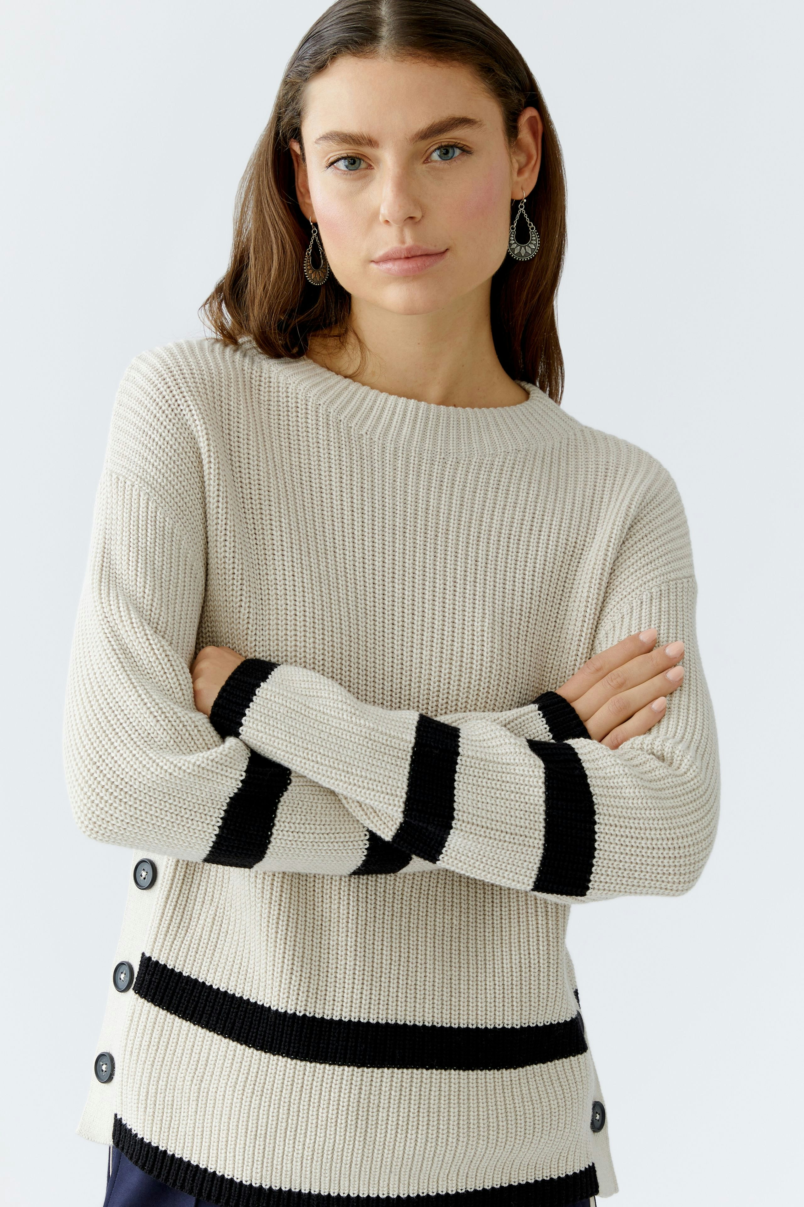 Casual women's pullover: A woman in a beige pullover with black stripes and button details, arms crossed.