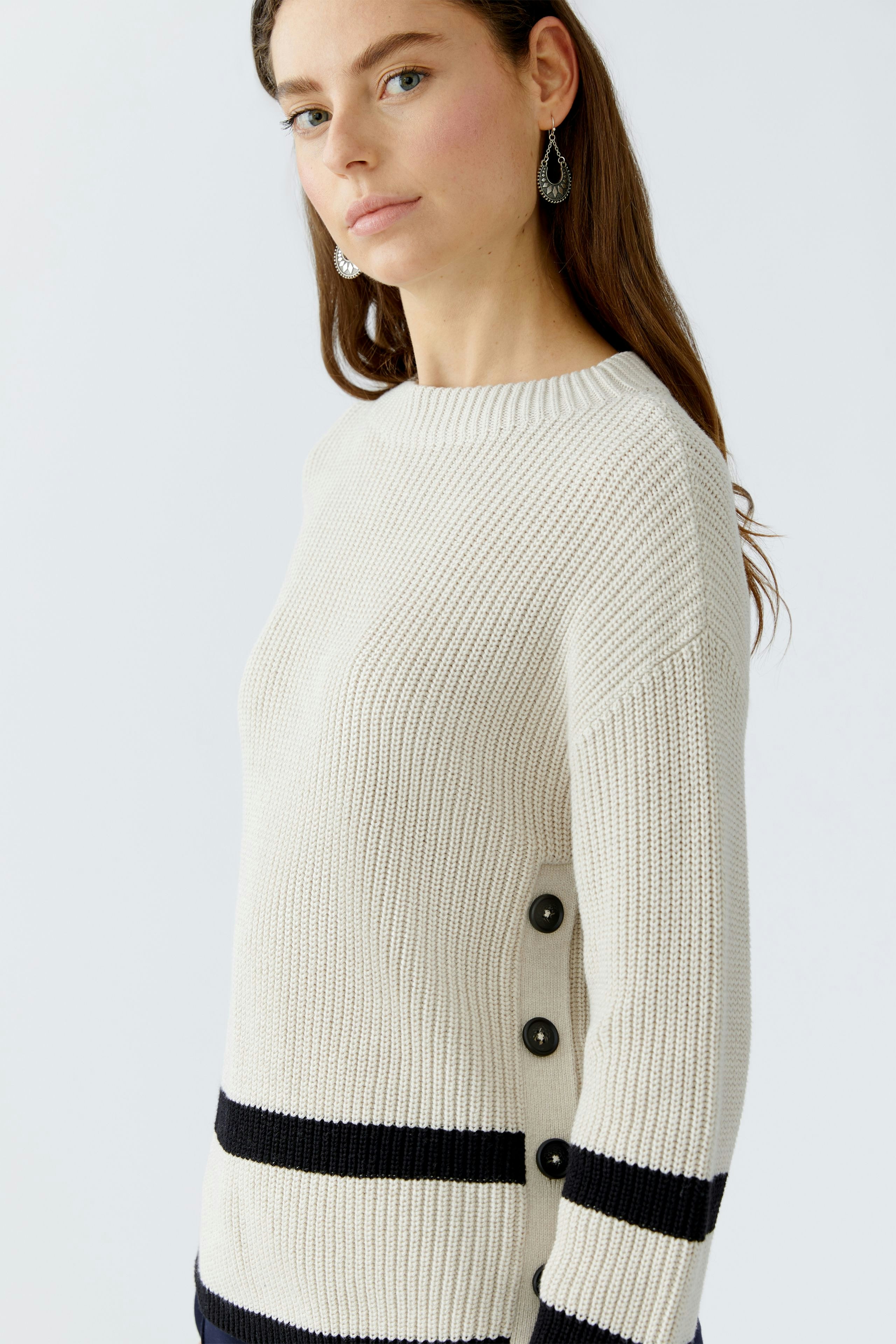 Casual women's pullover: A woman in a cream pullover with black stripes and button details.