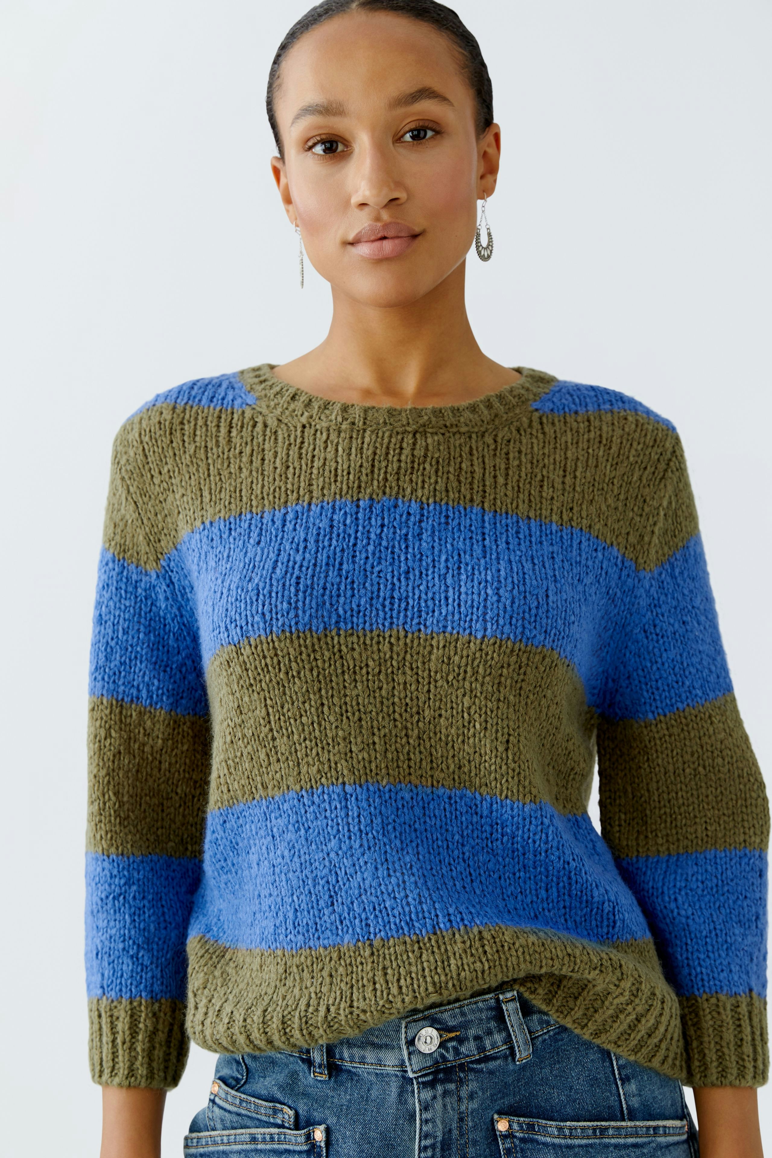 Damen-Pullover: Frau trägt einen gestreiften Pullover in Blau und Olivgrün, lässig kombiniert mit Jeans.