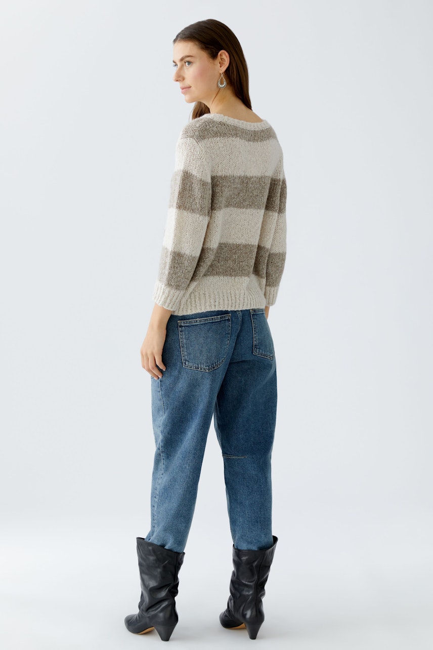 Casual women's pullover: A woman in a striped pullover with relaxed fit and blue jeans, facing away.