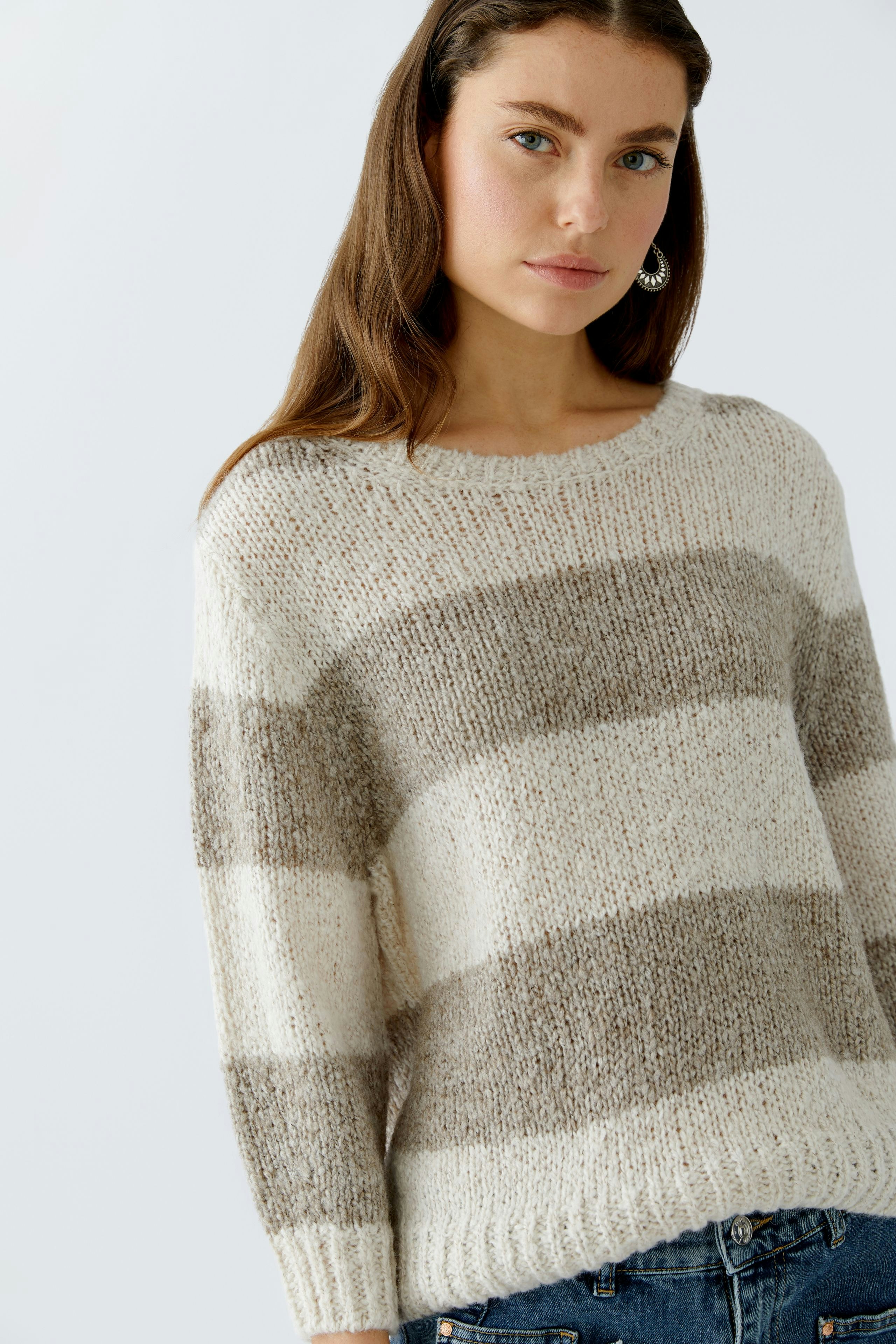 Casual women's pullover: Young woman in a striped knit pullover with neutral tones, smiling confidently.