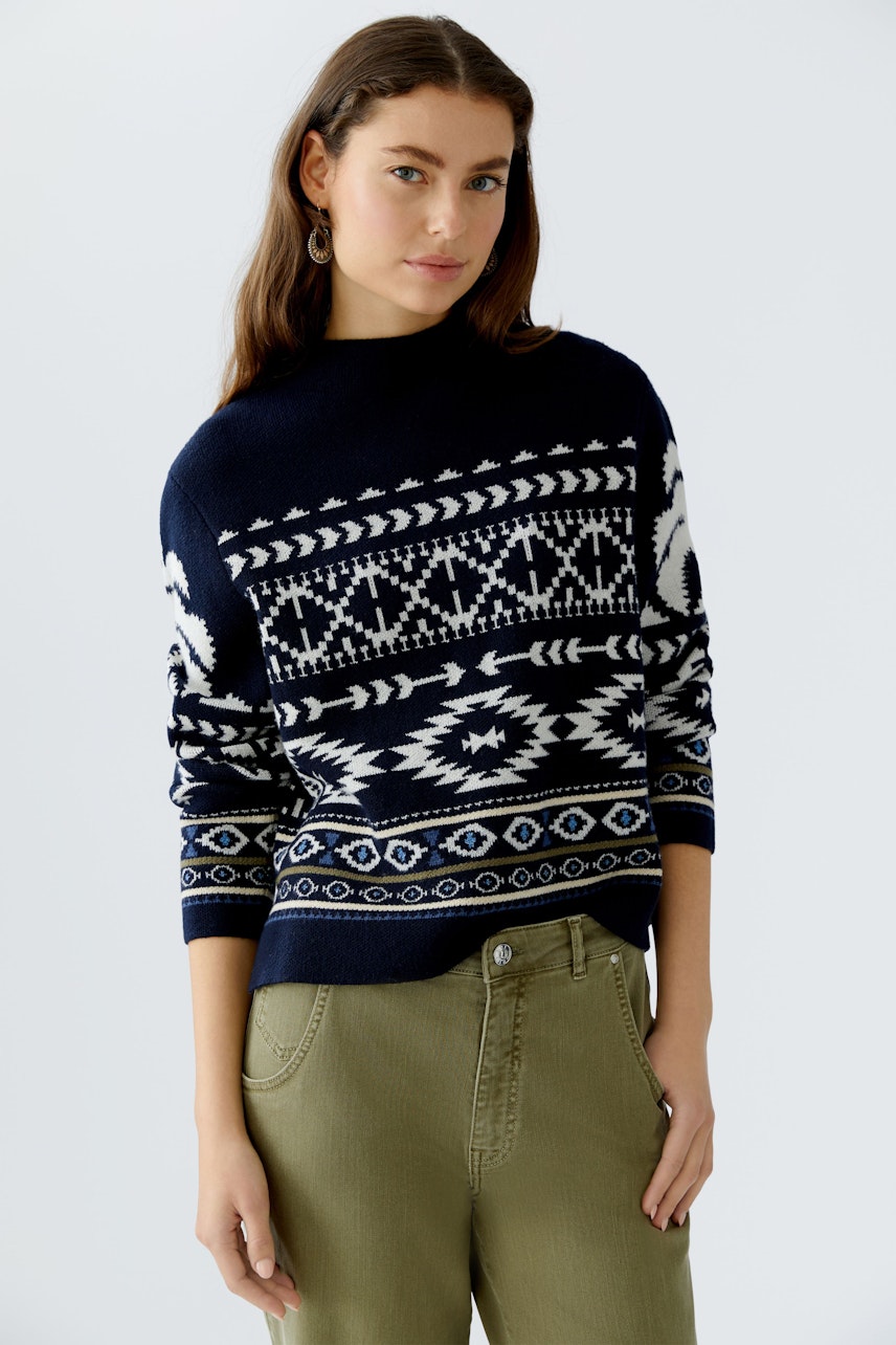 Damen-Pullover: Frau trägt einen blauen Pullover mit weißem Muster und lässigen Hosen.