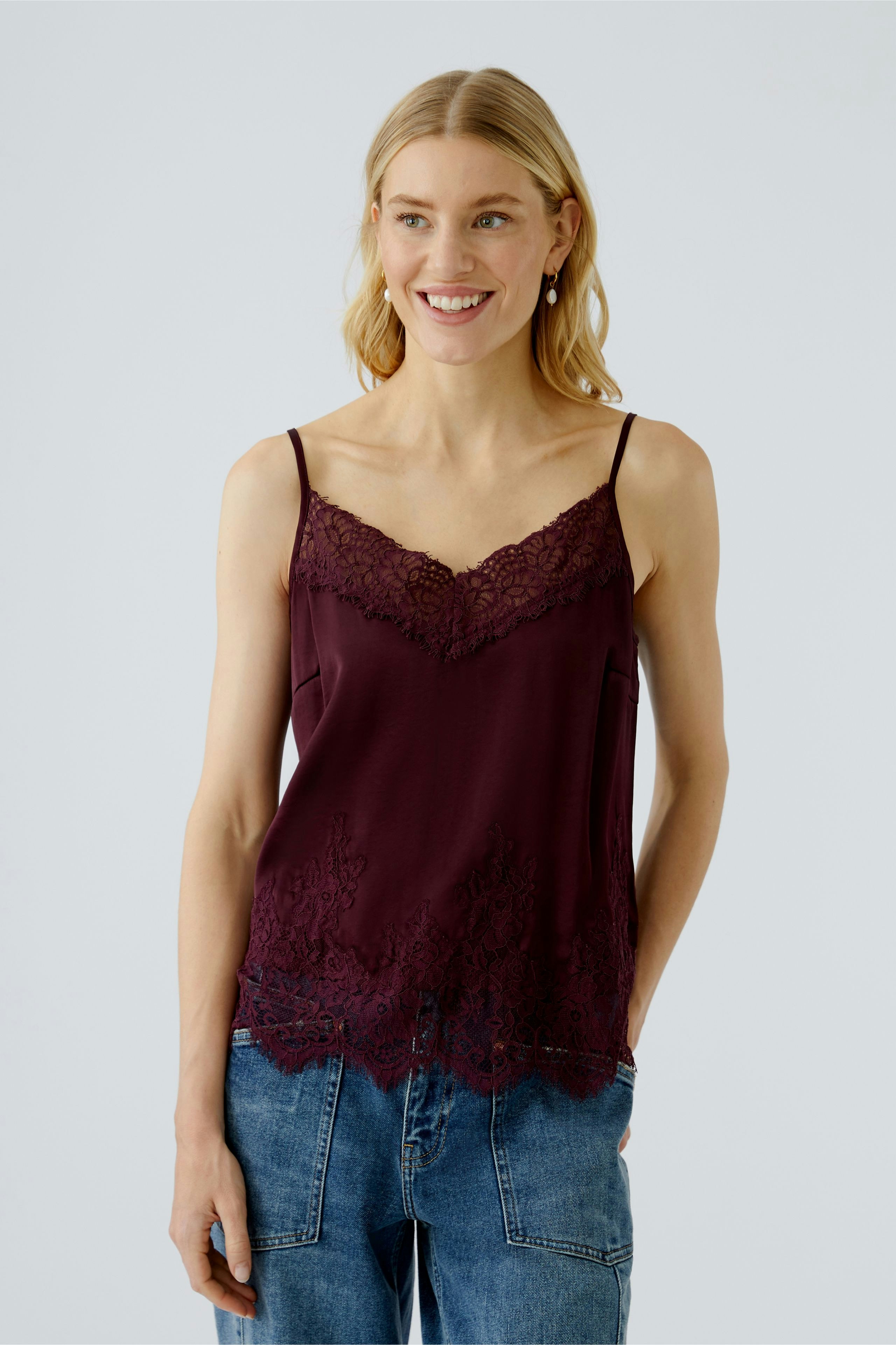 Casual women's top: Young woman in a burgundy lace-trimmed camisole paired with relaxed denim.