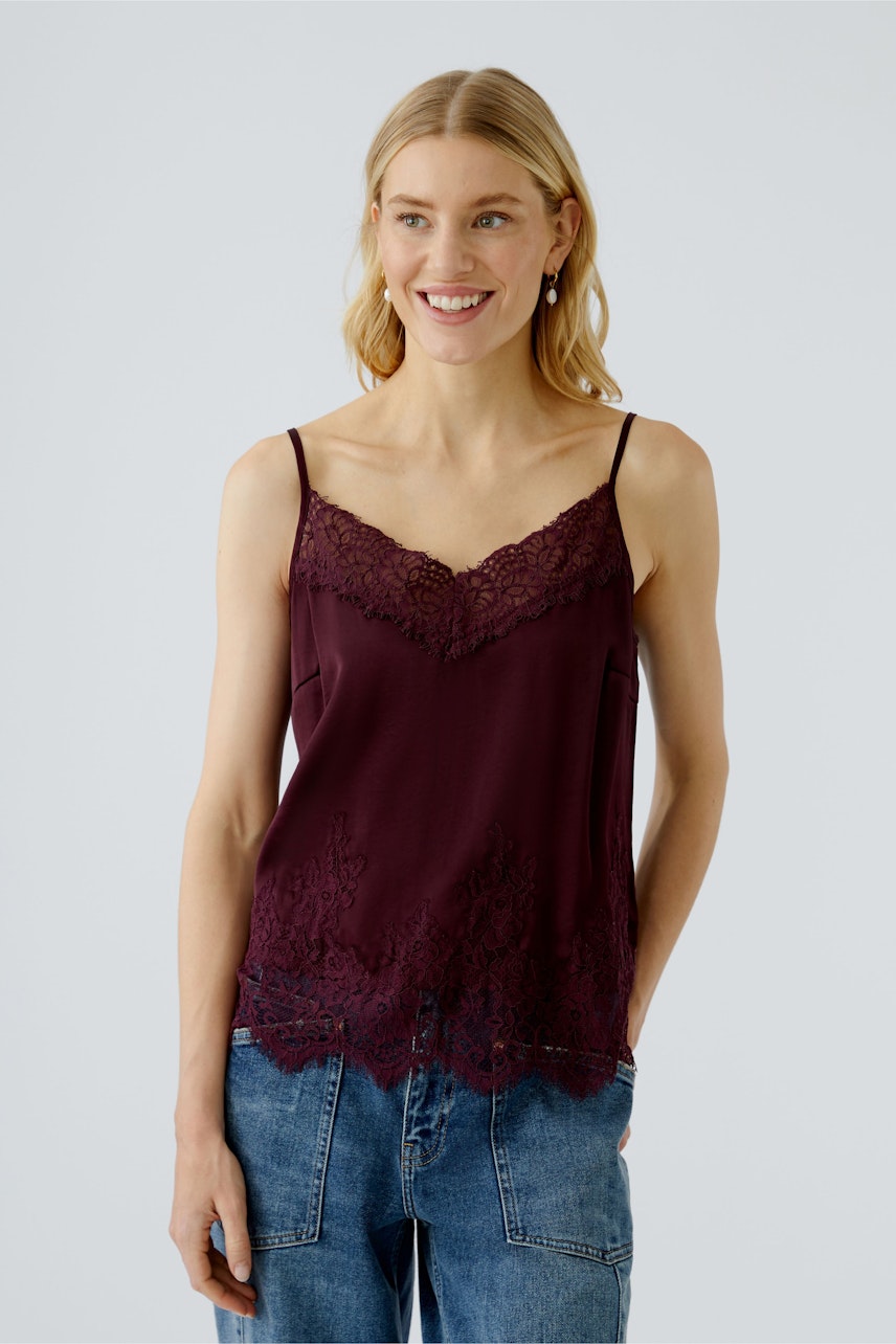 Damen-Top: Junge Frau trägt ein bordeauxfarbenes Spaghetti-Top mit Spitze und lässigen Jeans.