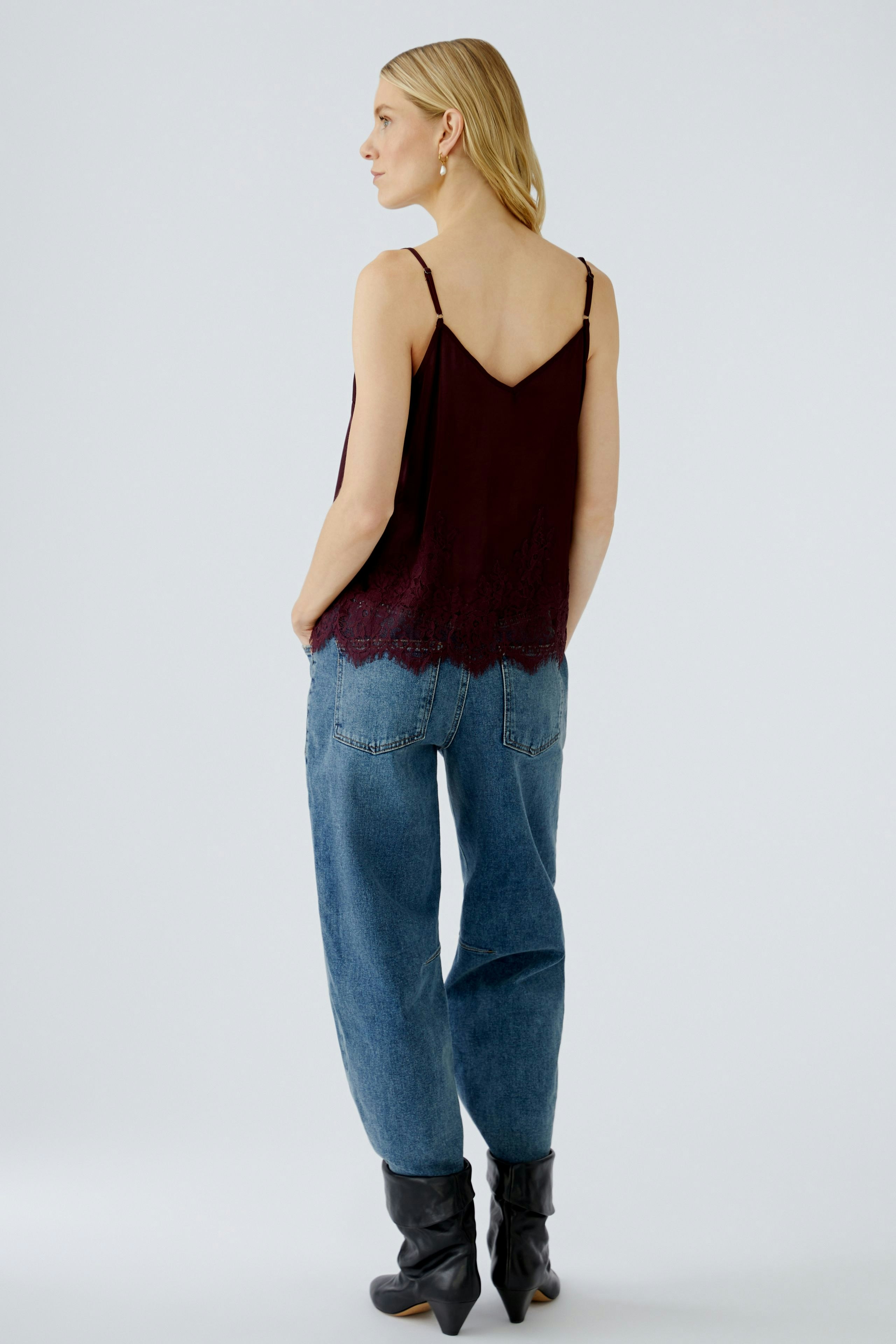 Casual women's top: Young woman in a burgundy tank top with lace detailing and relaxed-fit jeans.