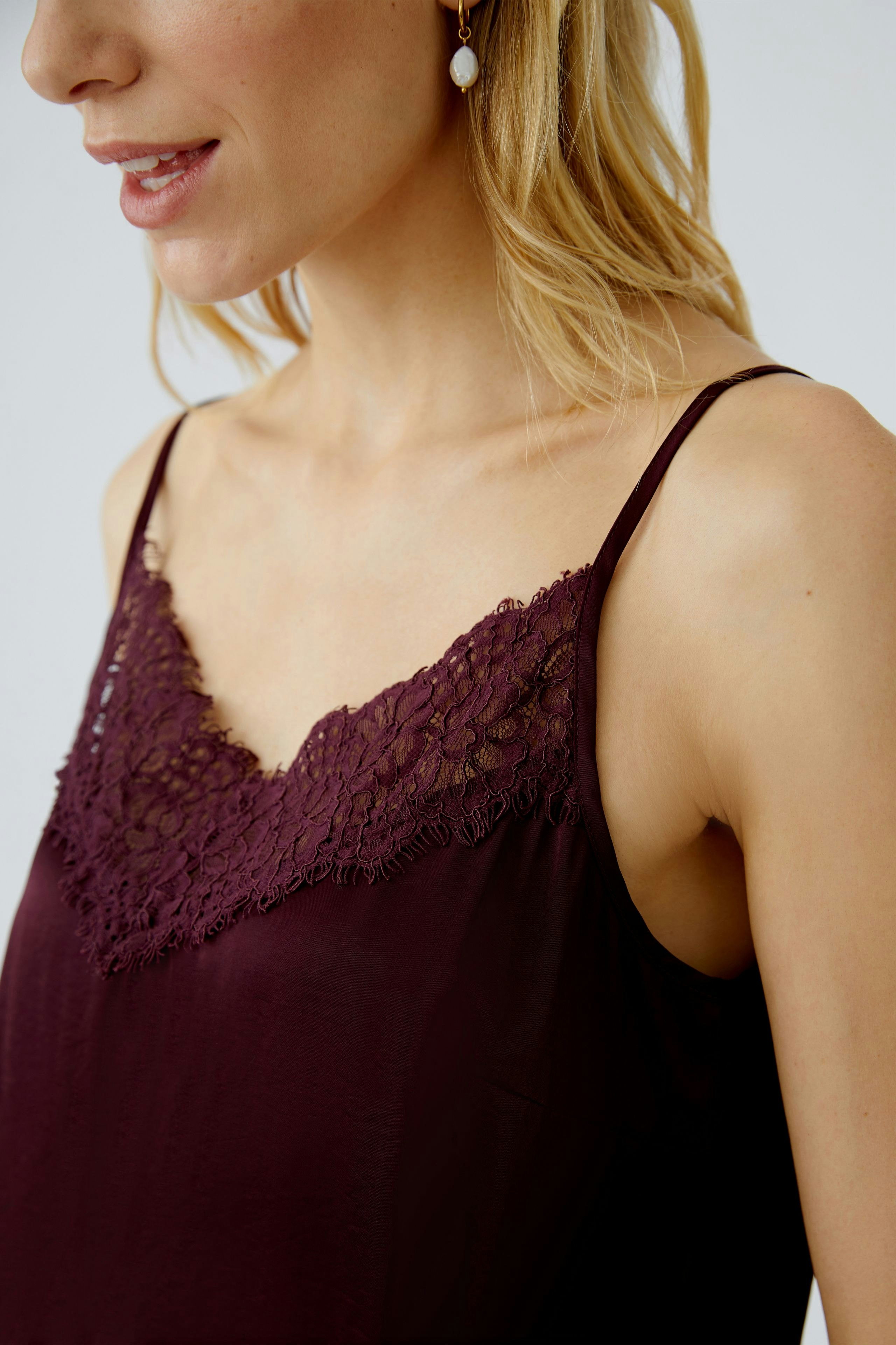 Casual women's top: Woman in a burgundy camisole with lace detailing, showcasing a relaxed style.