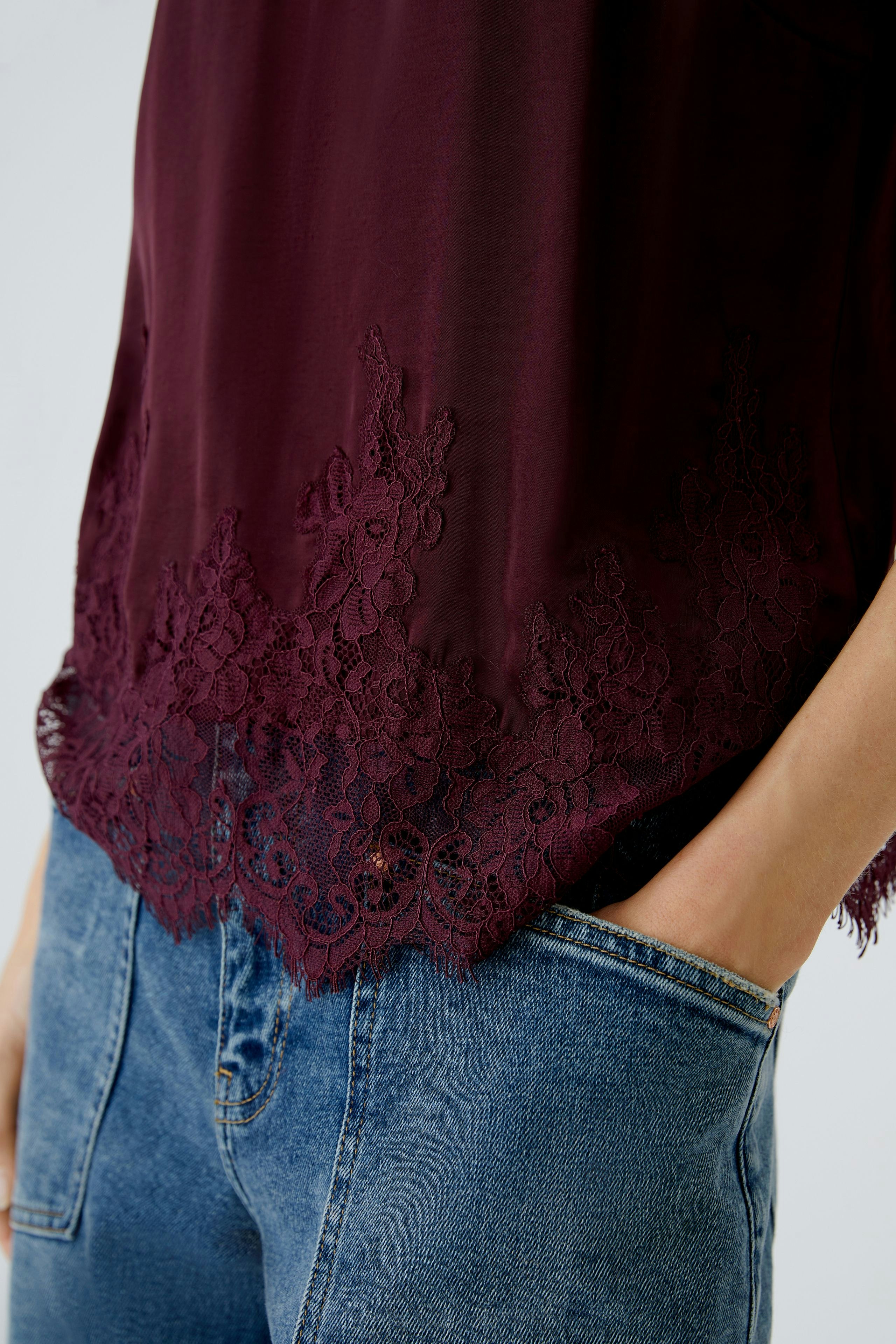 Casual women's top: Close-up of a woman wearing a burgundy top with lace detailing and relaxed jeans.