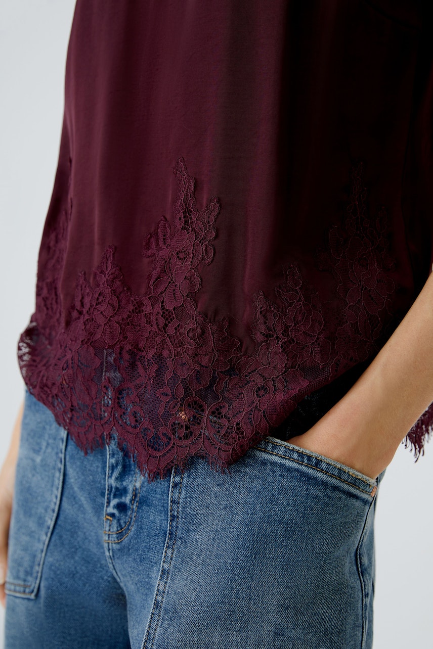Damen-Top in Bordeaux mit feiner Spitze am Saum, kombiniert mit lässigen Jeans.