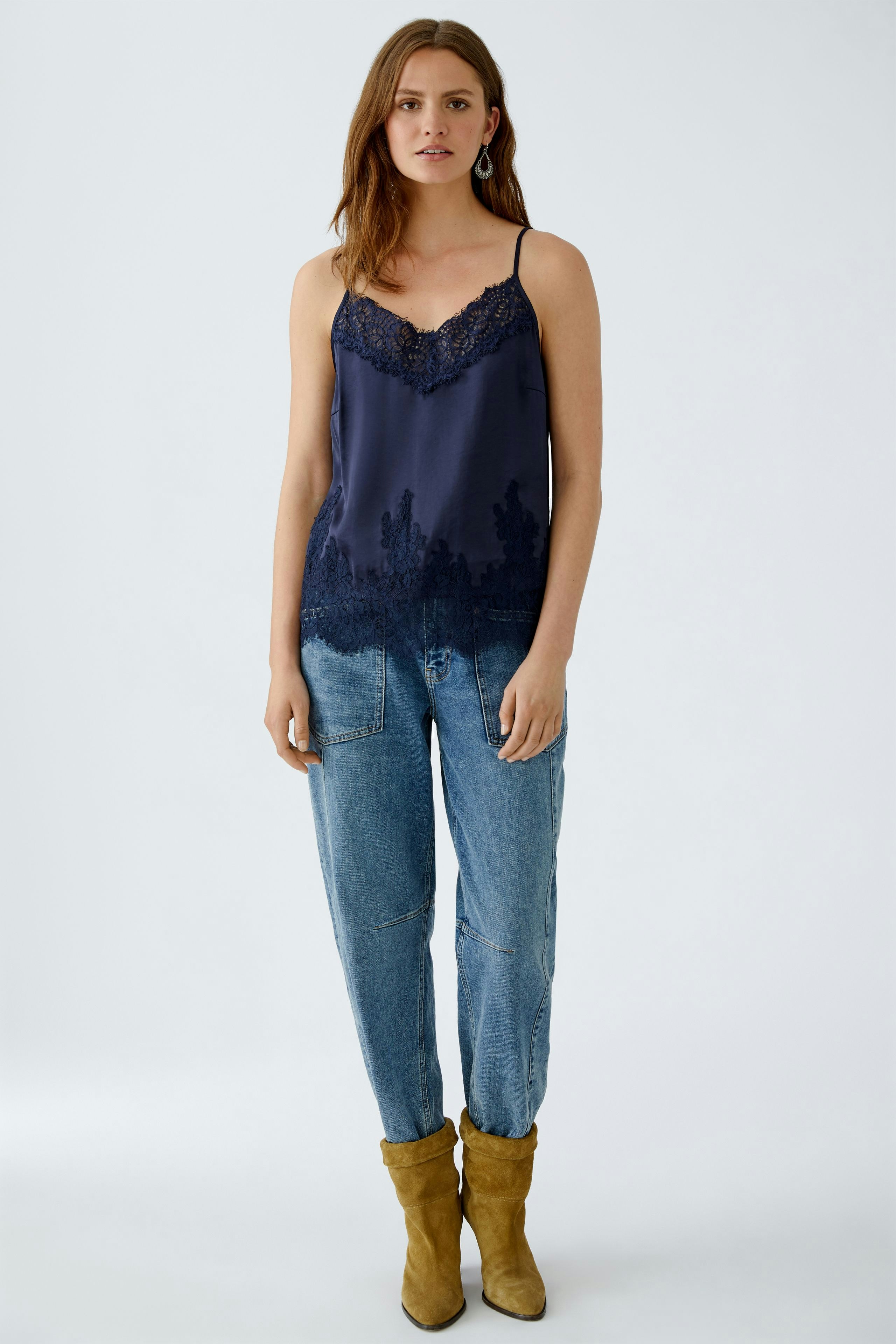 Casual women's top: Young woman in a navy lace-trimmed tank top paired with relaxed jeans.