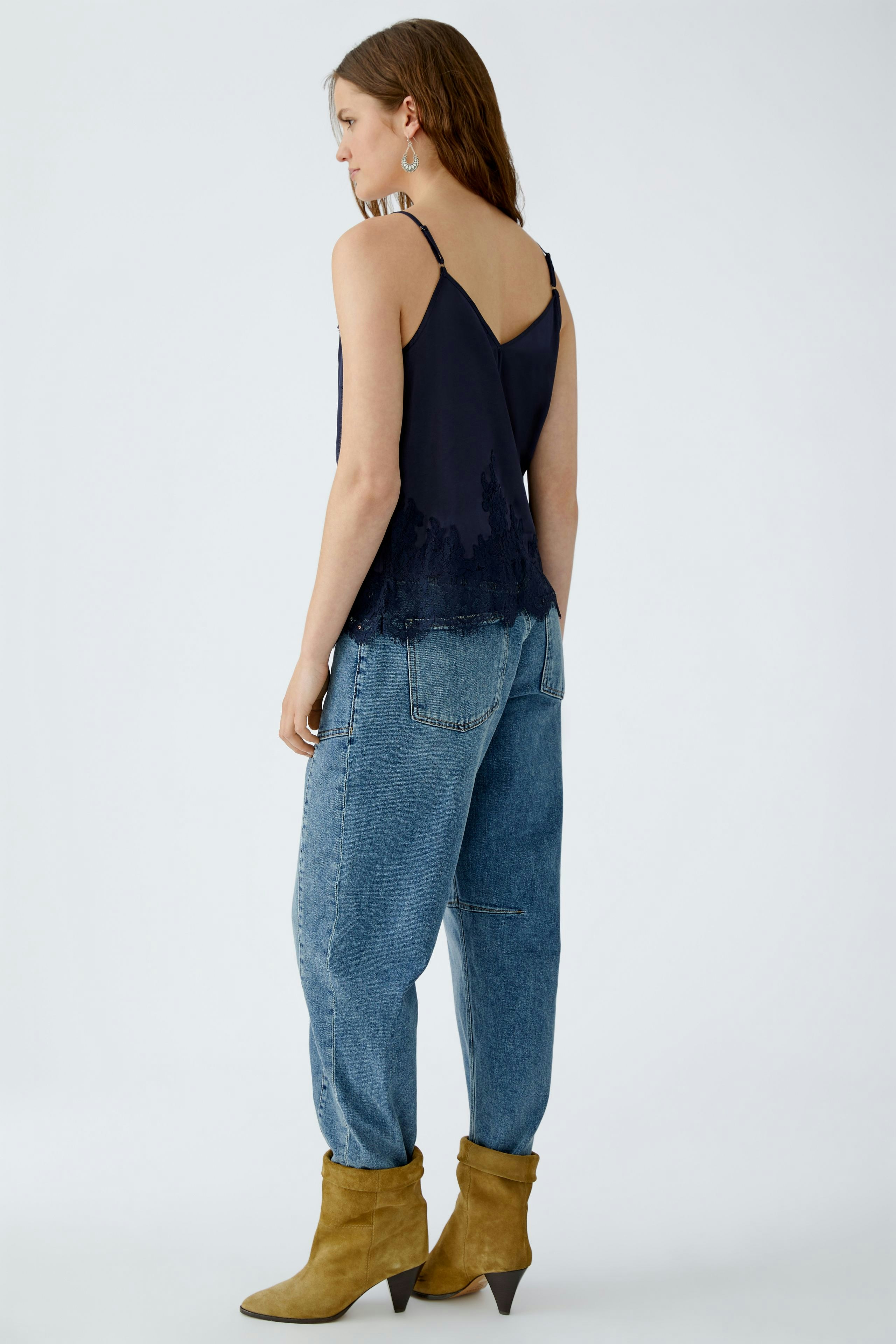 Casual women's top: A woman in a navy tank top with lace details, paired with relaxed jeans and boots.